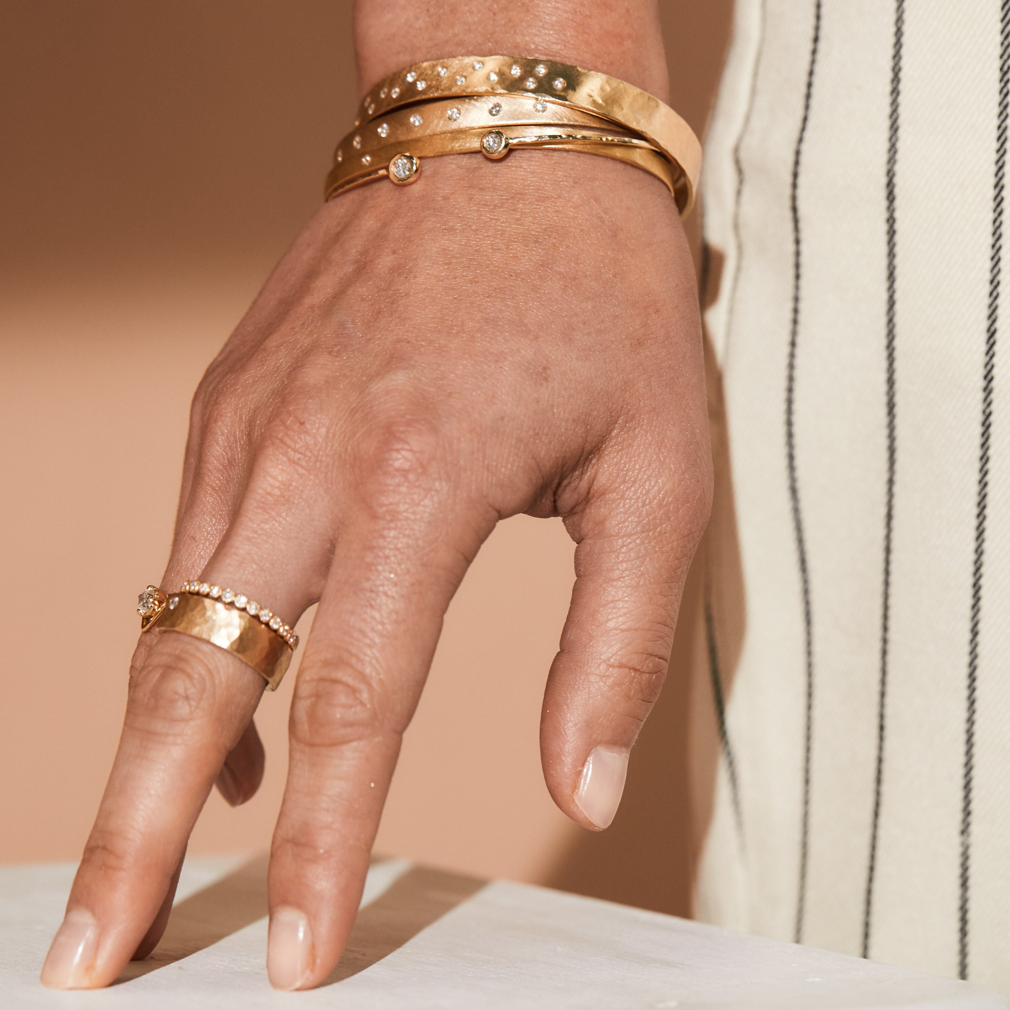 Close up of hand wearing 14k yellow gold with diamonds layered jewelry rings and bracelets lifestyle shot with a neutral background