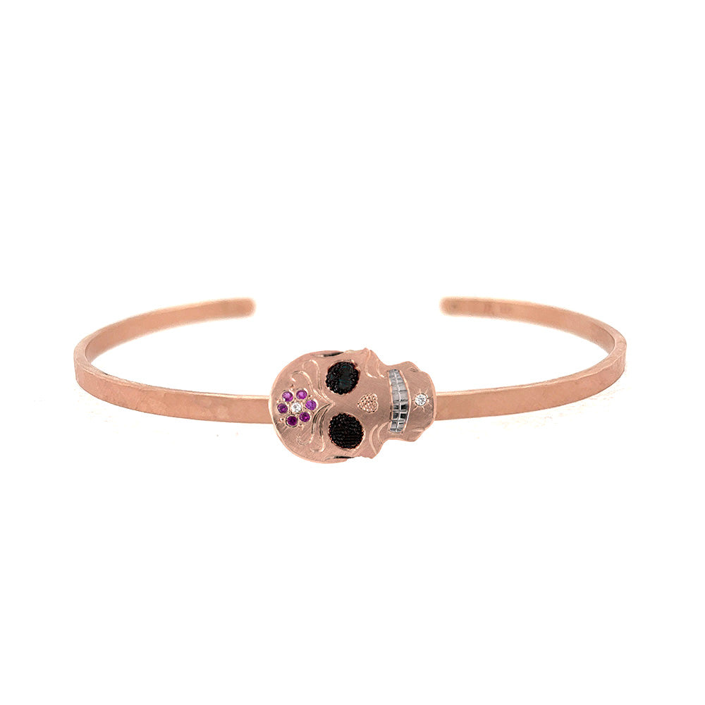 14k rose gold skull-shaped cuff bracelet with gemstones and rhodium brightened teeth on a white background