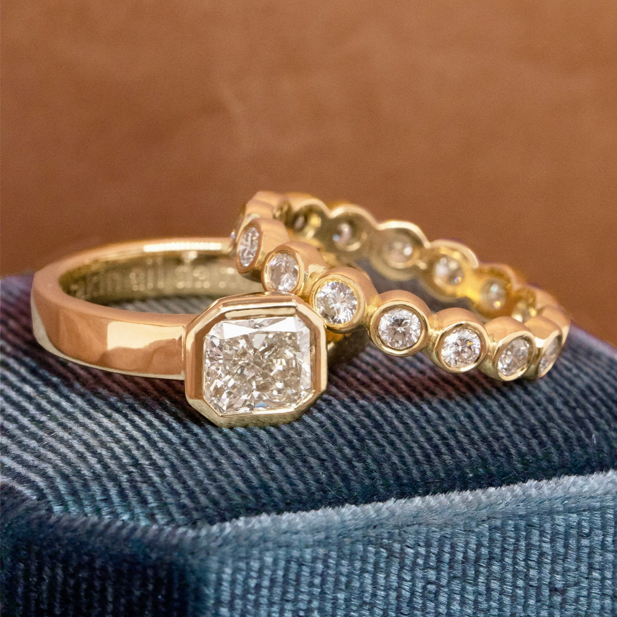 Thick band eternity and asscher cut white diamond solitaire engagement wedding band set on blue velvet box blurred brown background
