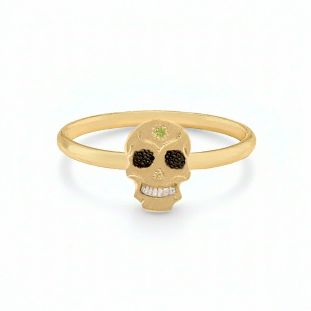 14k Gold handcut skull ring with black eye sockets and a green gemstone on a white background