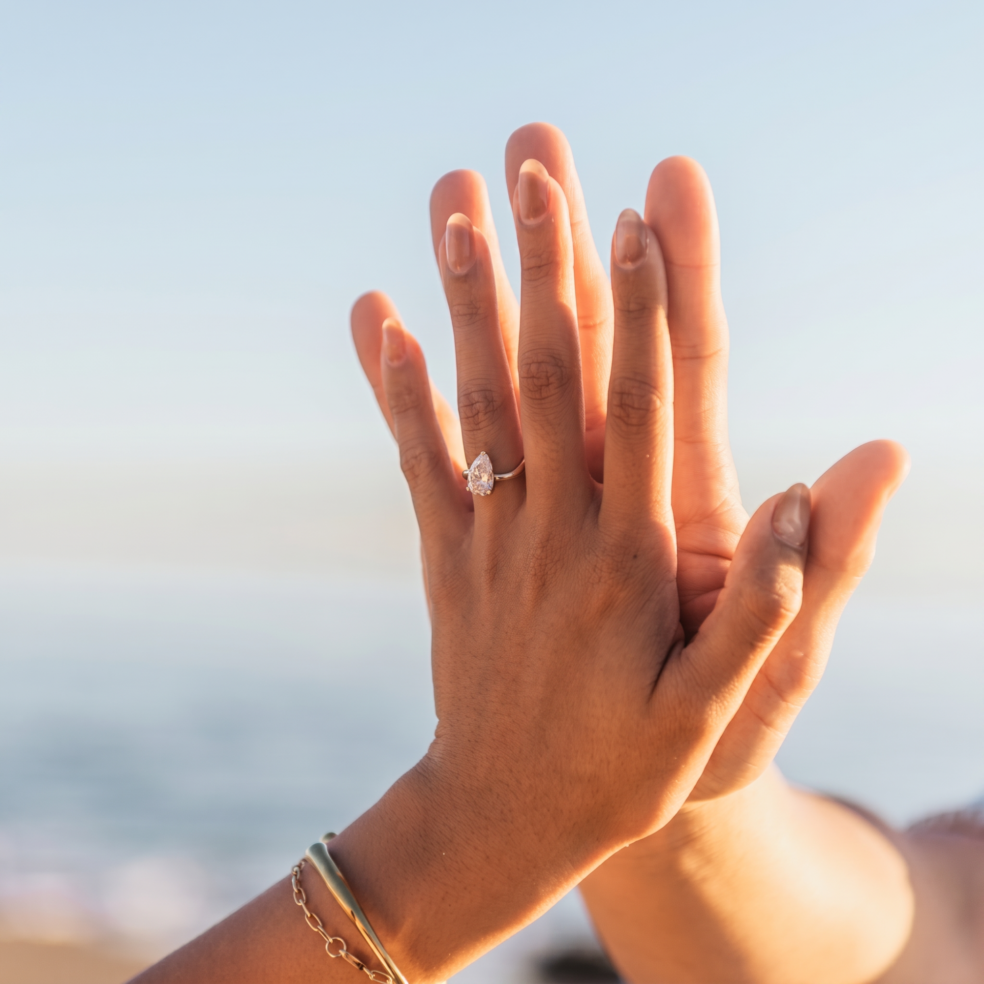 Solitaire pear cut diamond engagement ring with prong set asymmetric band in 14k yellow gold, lifestyle shot on a model's hands