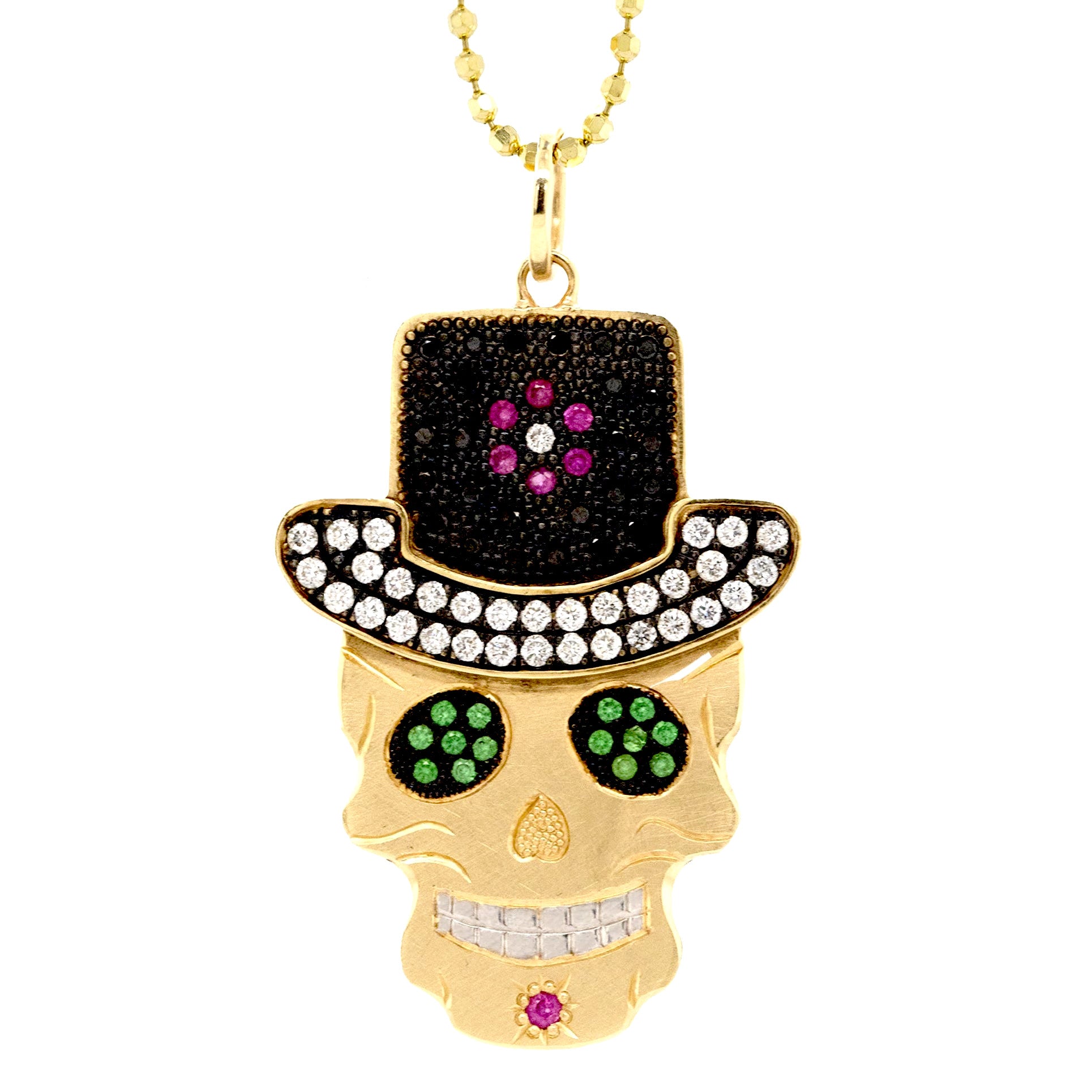Closeup of handcut 14k yellow gold skull pendant wearing black diamond encrusted top hat and white diamond brim. Green gemstone eyes rhodium plated details close up on a white background