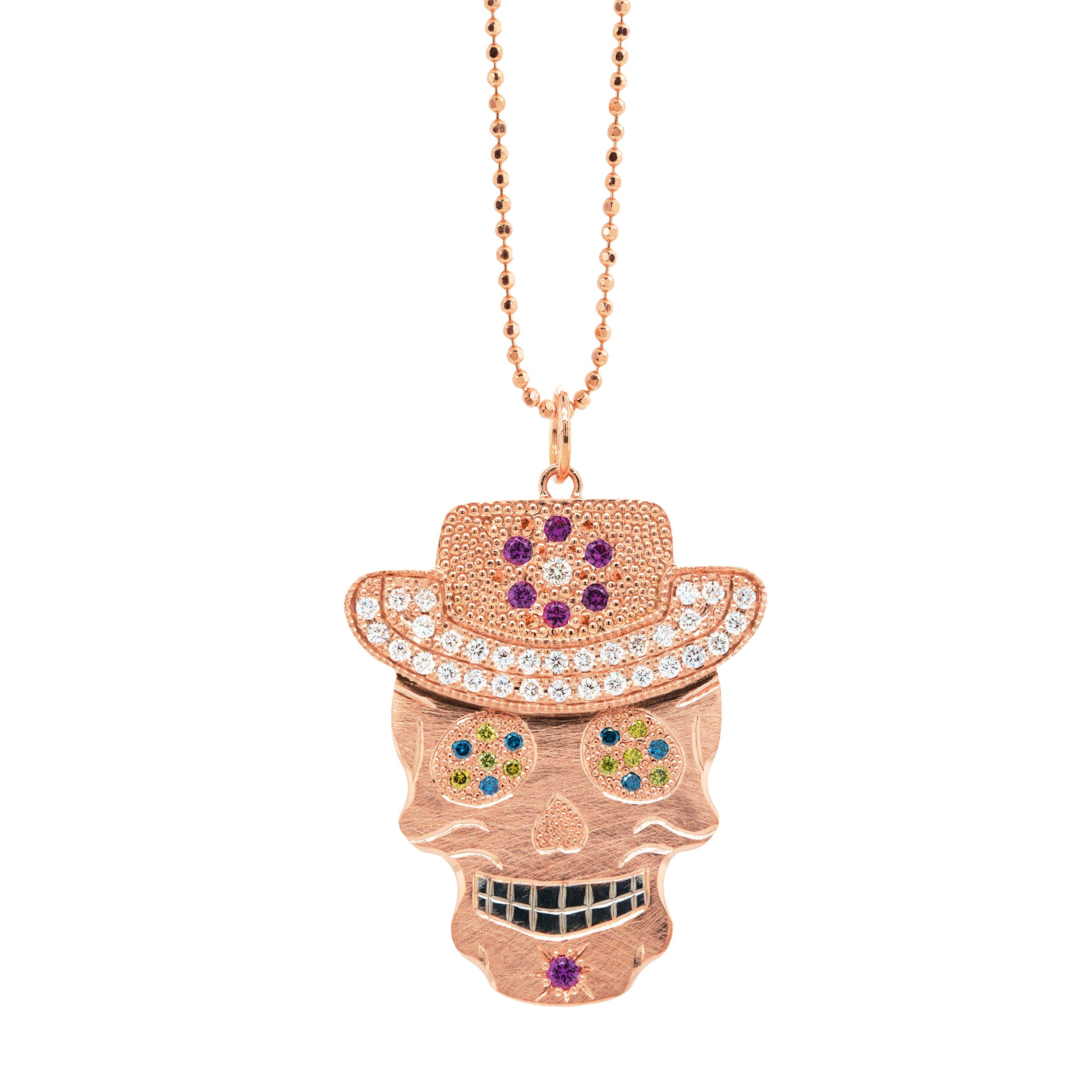 Gemstone encrusted sugar skull wearing cowboy hat in 14k rose gold with black rhodium darkened teeth. Extra large pendant in 14k solid yellow gold mixed diamond sapphires and Tzavorite. Fine detail engraving highlights features. Hat of flower clustered jewels in mixed colors. Eyes with green Tzavorite and blue sapphire pave set gemstone eyes. Large pink sapphire Flower pave set detail on hat. Shown on 2.0mm ball chain.