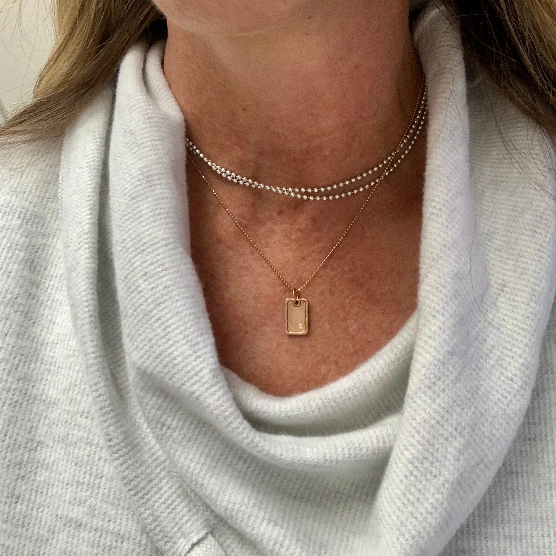 14k gold small DANA dog tag charm with one diamond on model