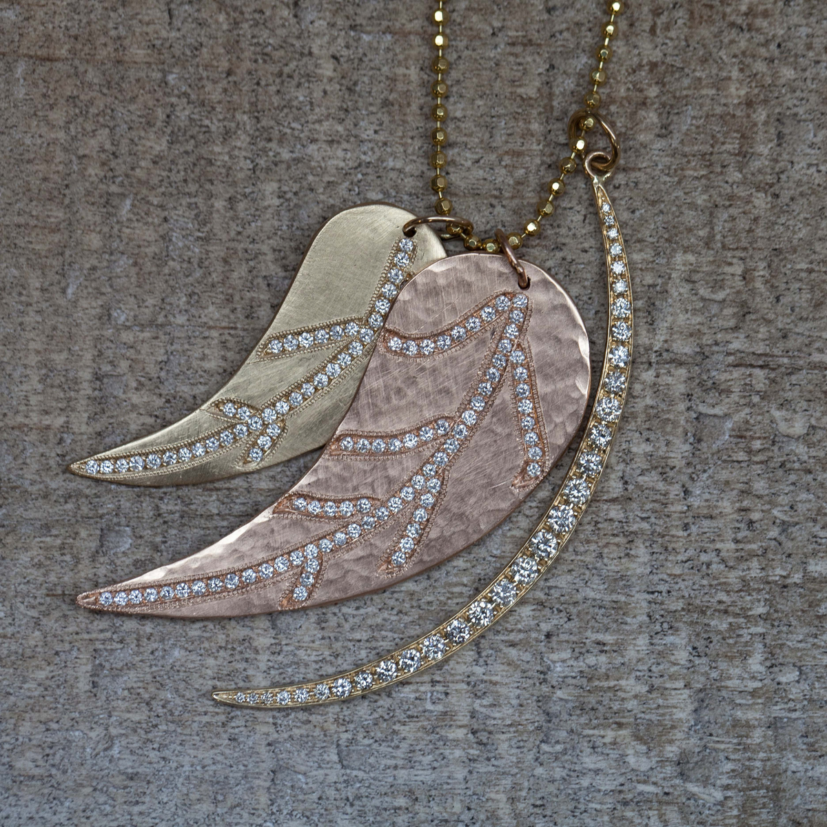 14k gold leaf pendant with pave set white diamonds stacked with other pendants on a dark background