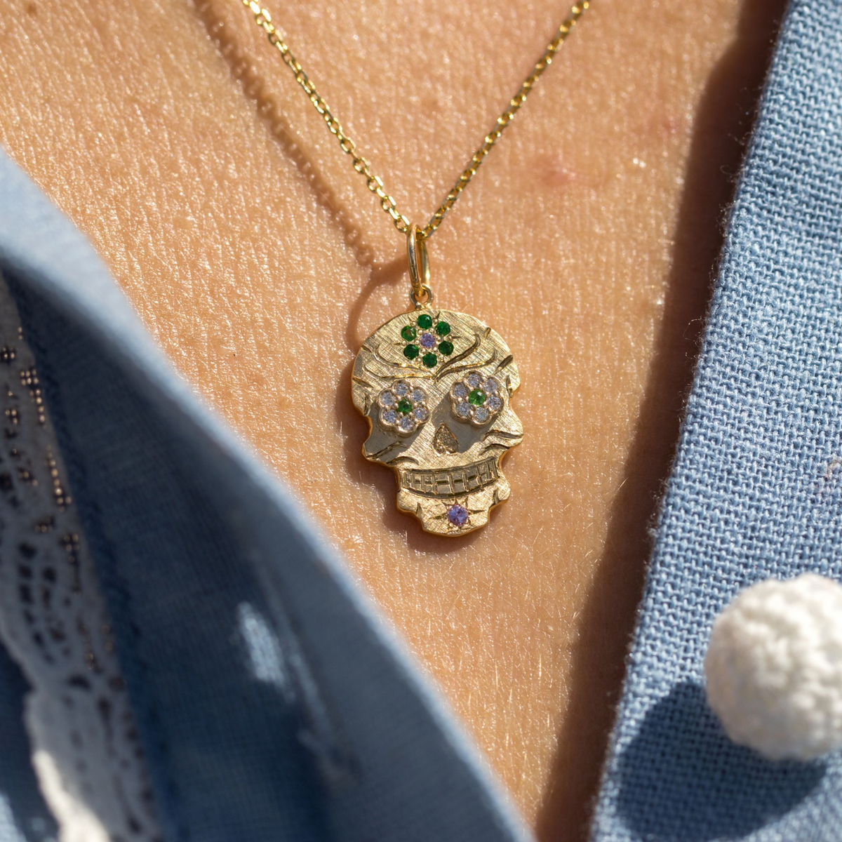 14k gold baby sized skor pendant with raised eyes and flower on forehead in lifestyle shot