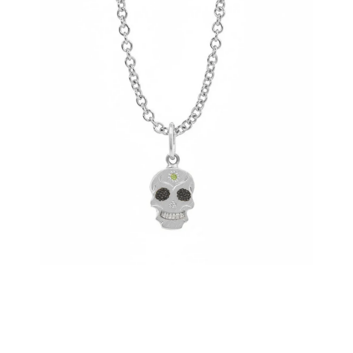 A Teeny Tiny collection white gold charm in the shape of a sugar skull with a round apple green diamond in the center, displayed on a gold chain against a white background.