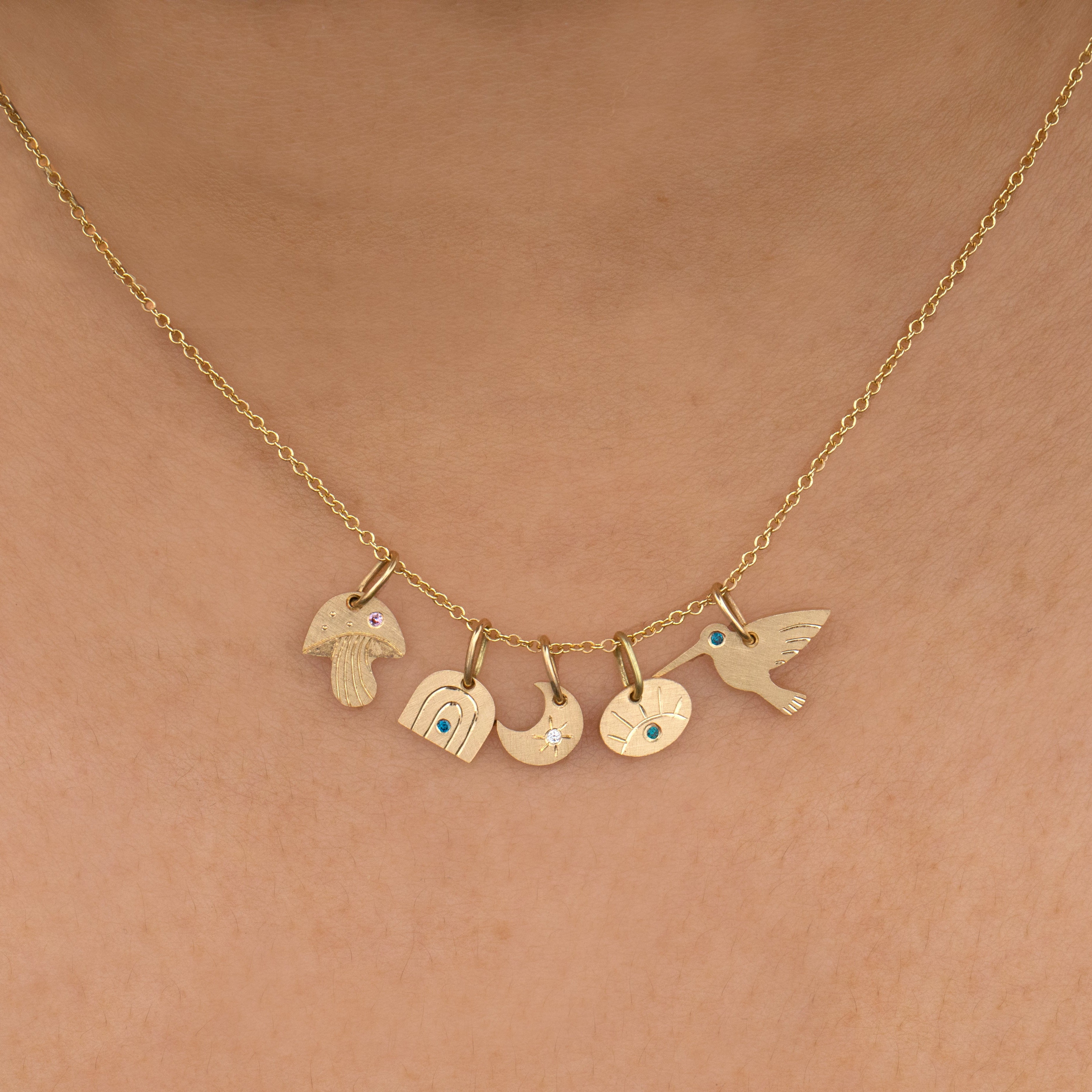 Gold necklace with various teeny tiny gold charms engraved cutout shapes with gemstones, charms layered on 1mm round link gold necklace on a person's neck