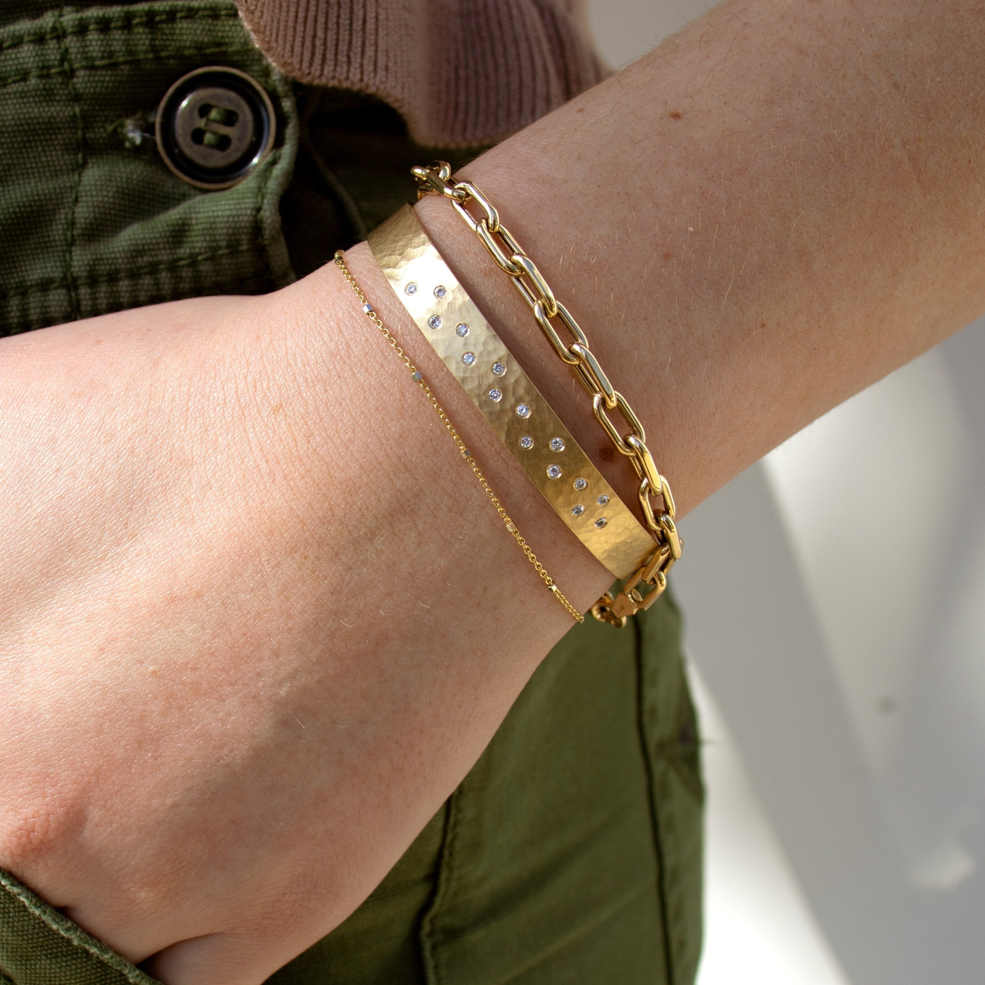 14k yellow gold 4.2mm mica thick paperclip link bracelet stacked with yellow gold hammered cuff with scattered white diamonds and a yellow and white gold chain bracelet on model in lifestyle shot