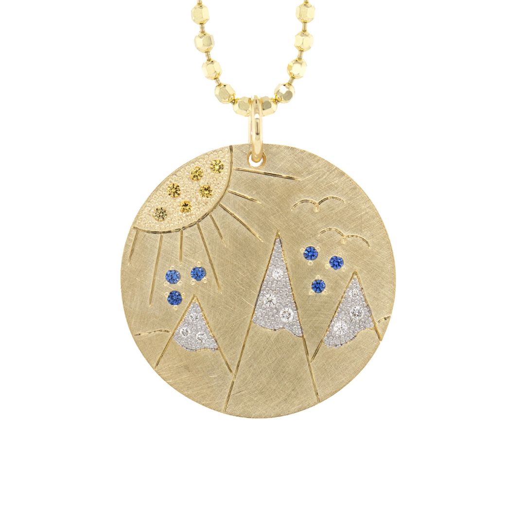 14k Gold round pendant with mountain etching with white diamond snow capped mountains and yellow and blue sapphires. 