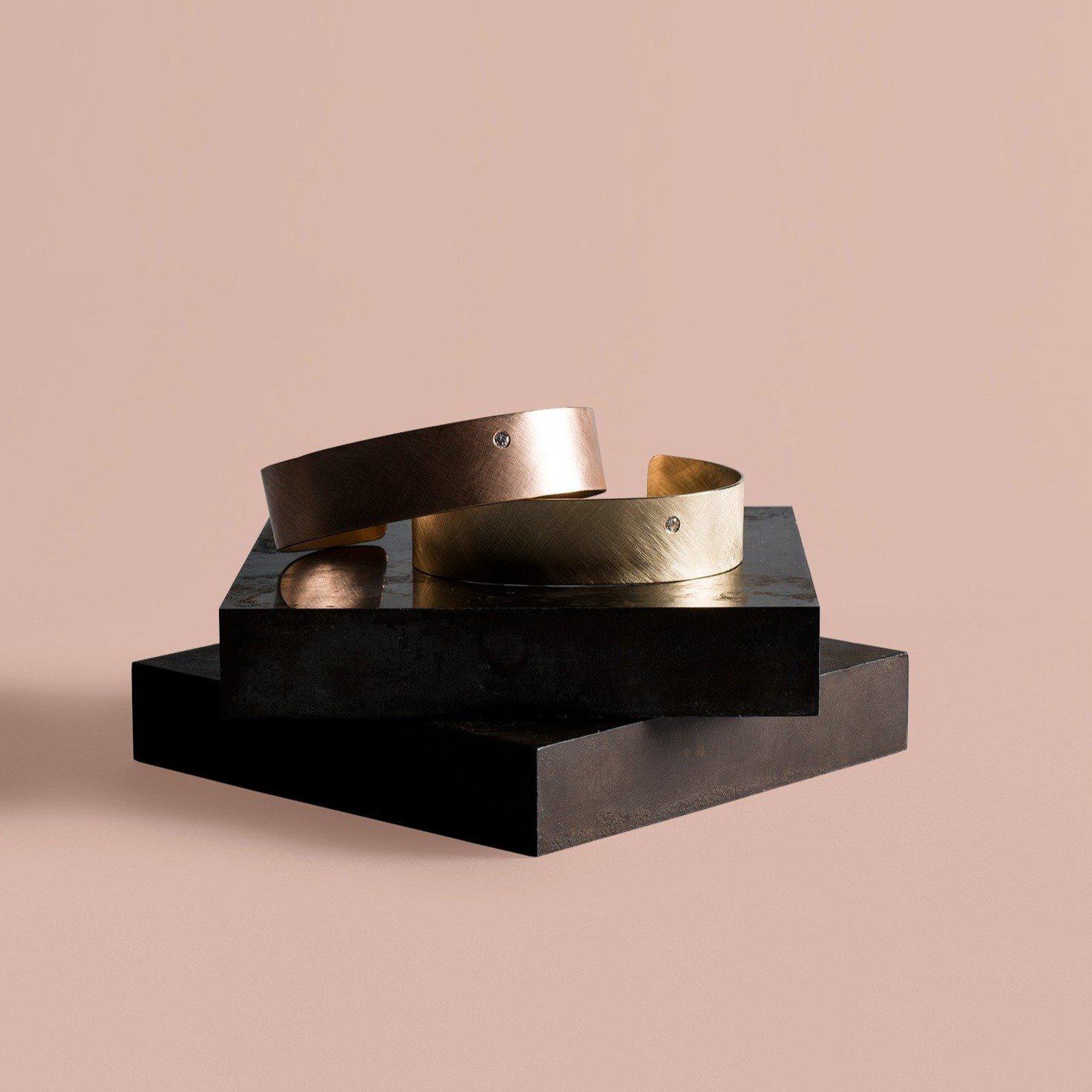 14k gold satin finished wide cuff bracelets with single offset white diamond on stone and taupe background