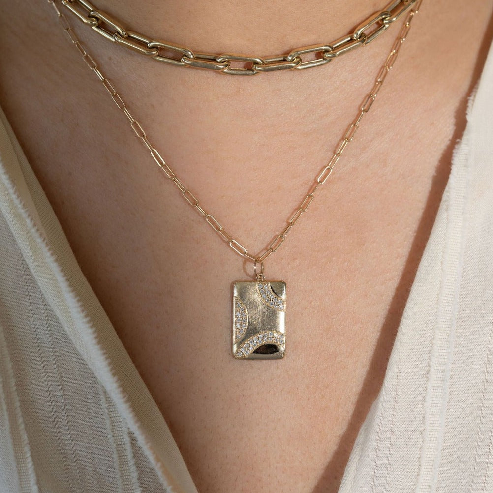 14k yellow gold rectangular pendant necklace with wavy diamond accents and a mix of shiny and satin finishes on diamond cut ball chain on a lifestyle shot paired with mica chain