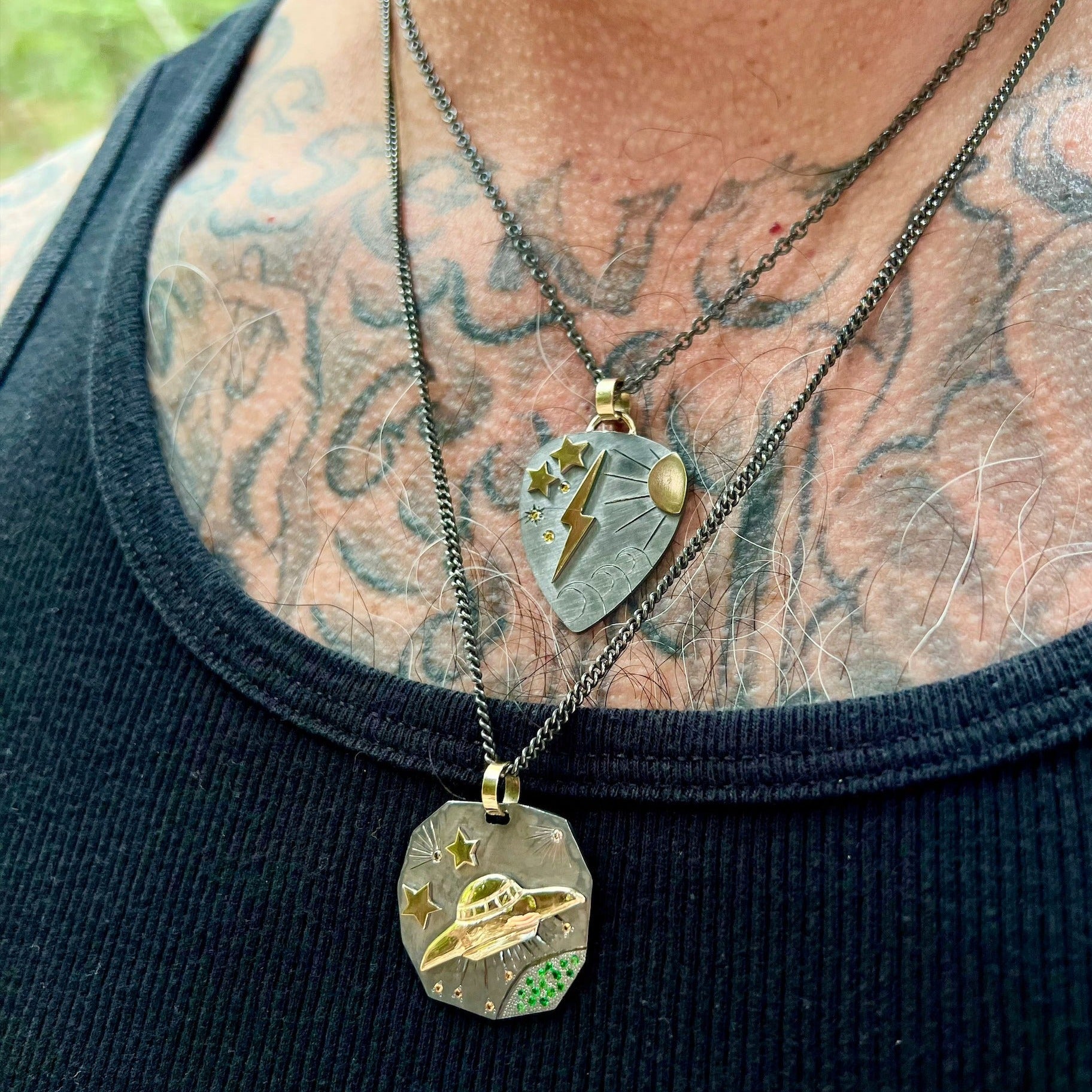 hammered blackened sterling silver pendant with 14k yellow gold ufo and stars with etching and colored gemstones stacked with blackened silver guitar pic pendant with 14k yellow gold accents on model in lifestyle shot