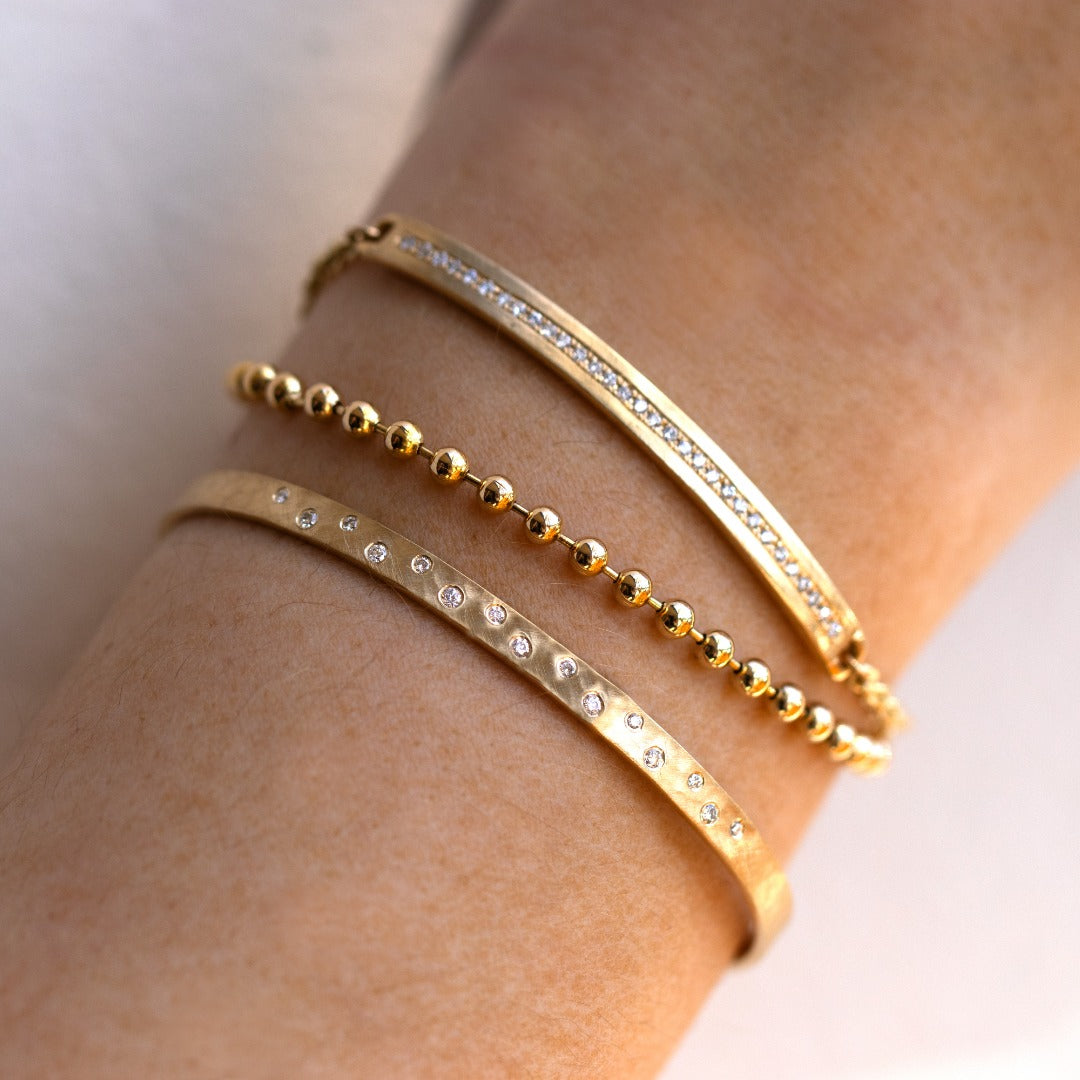 14k yellow gold pave set white diamond bar bracelet with a rolo chain stacked with a ball chain and hammered cuff bracelet with scattered white diamonds on model in lifestyle shot
