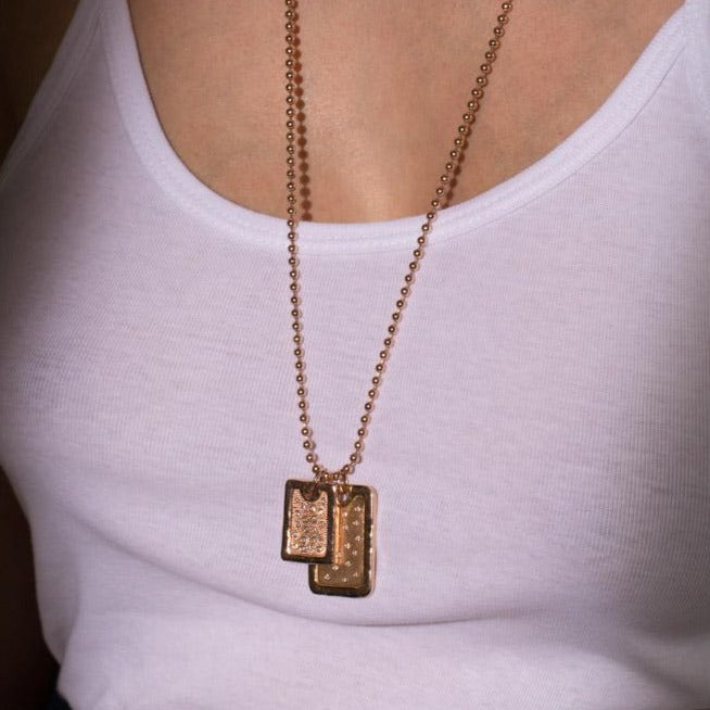 14k yellow gold necklace with two rectangular dog tag pendants hanging from a ball chain on a white shirt lifestyle shot shown on model.