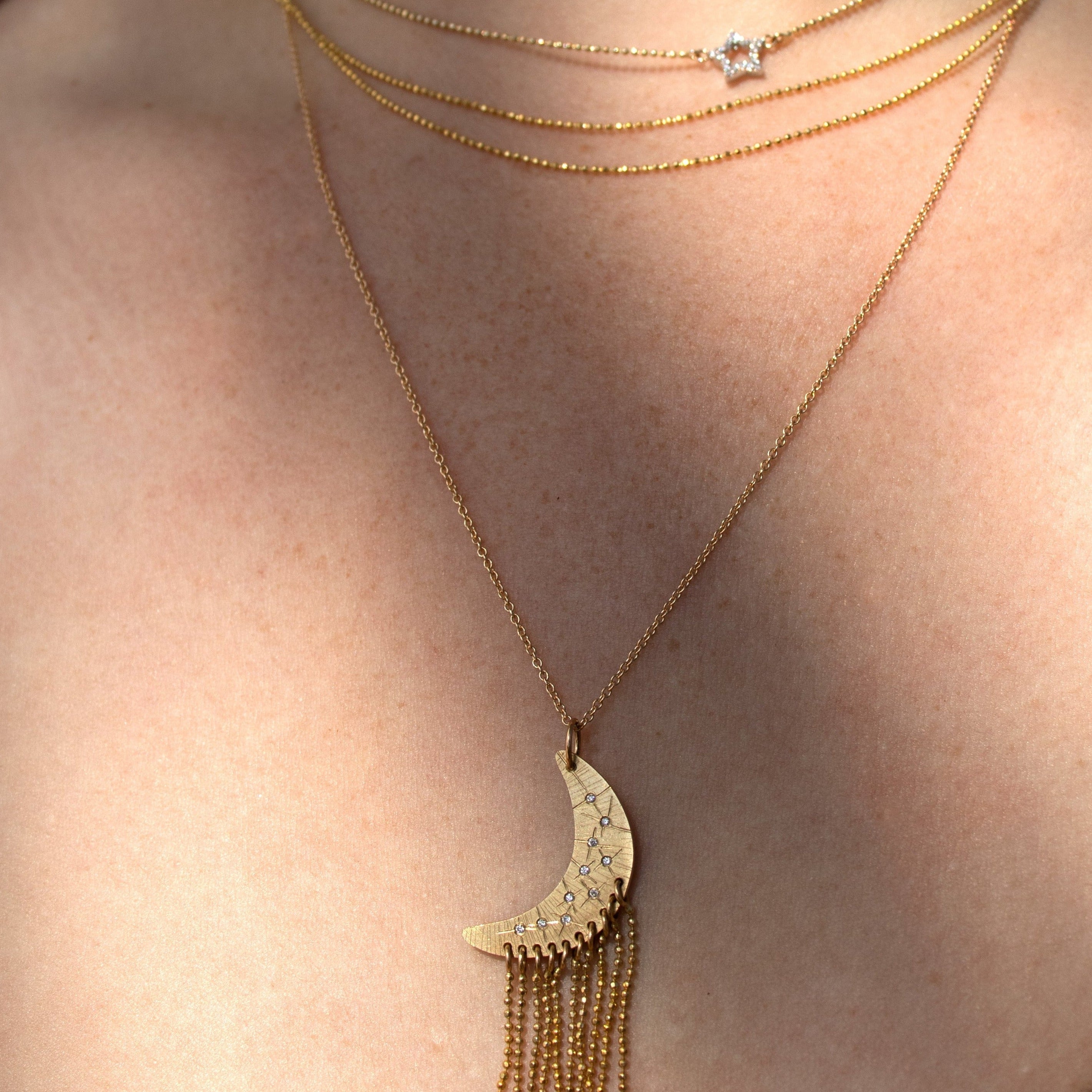 Close-up of a person wearing multiple gold necklaces with a star and crescent moon pendant.