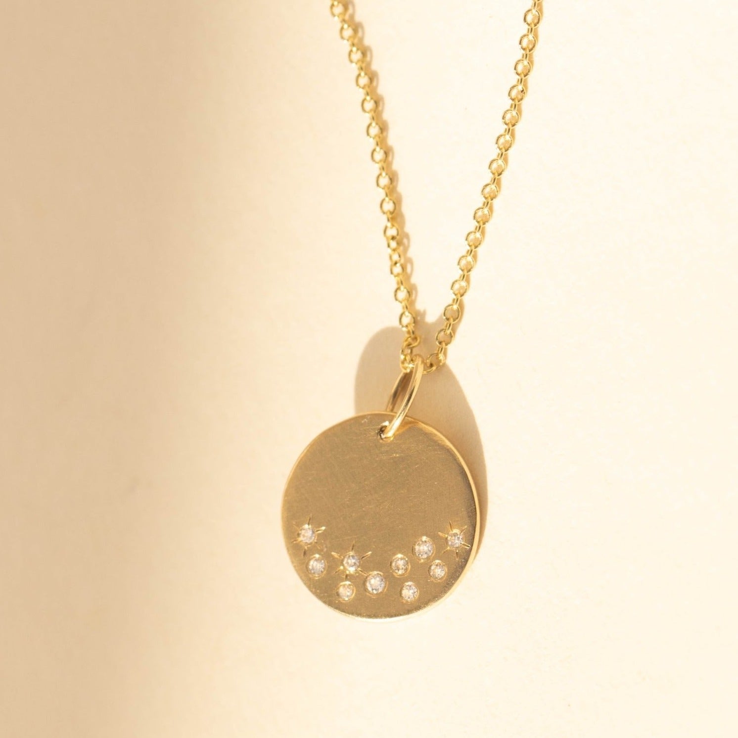 14k yellow gold round pendant with white diamond starburst on rolo chain  on a beige background