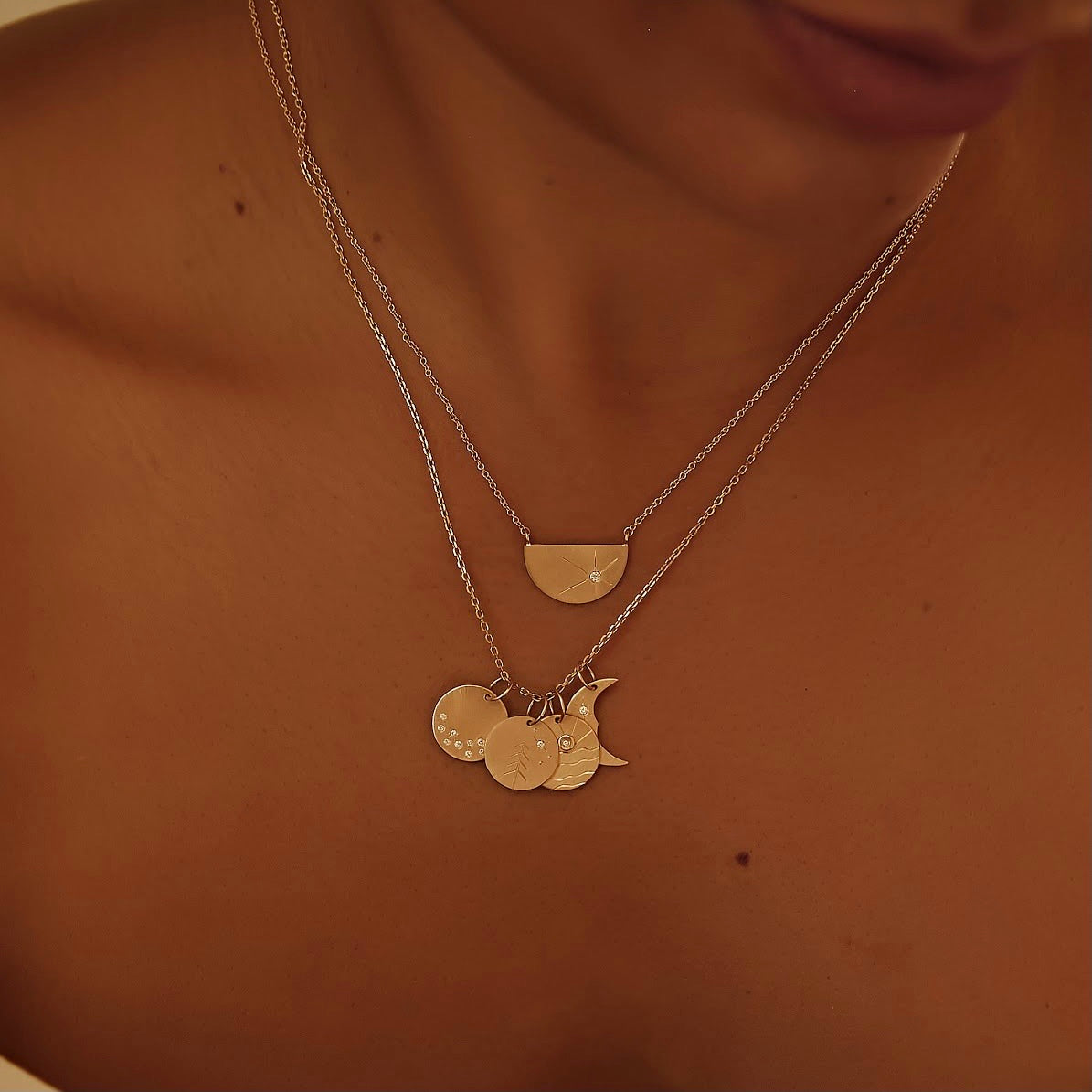 14k gold pendants stacked on rolo chain on model in lifestyle shot featuring round charm with white diamonds and starburst etching