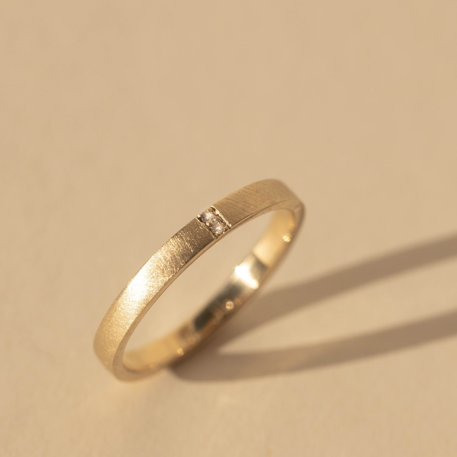14k yellow gold stacker ring featuring two white diamonds set side by side in a satin finished band on a tan background
