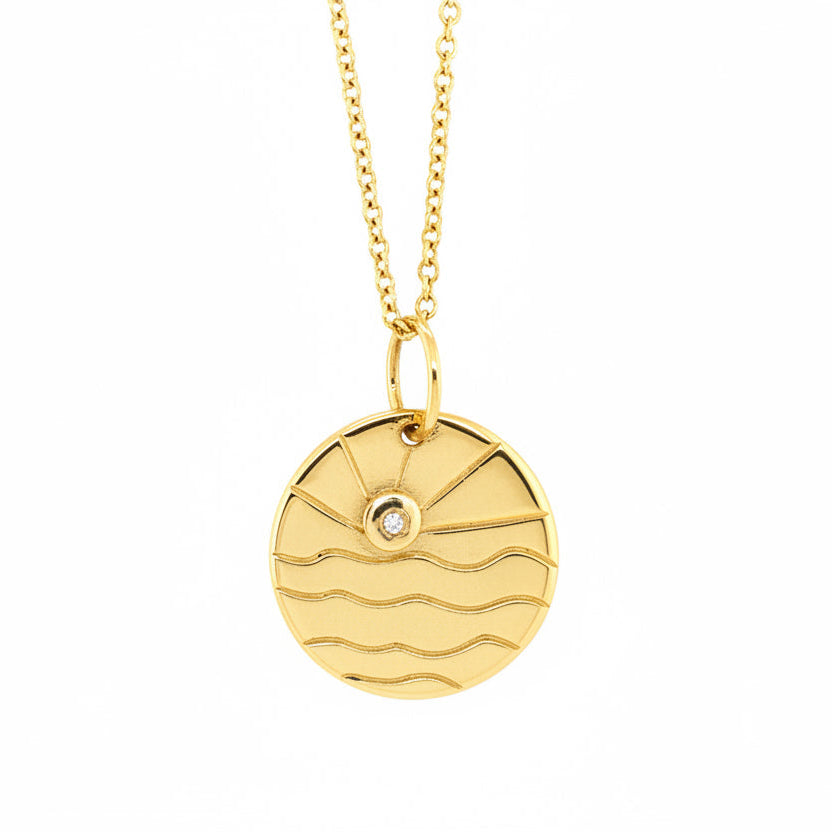 14k yellow gold circular pendant featuring wavy designs with a bezel set white diamond sunburst on a rolo chain on a white background
