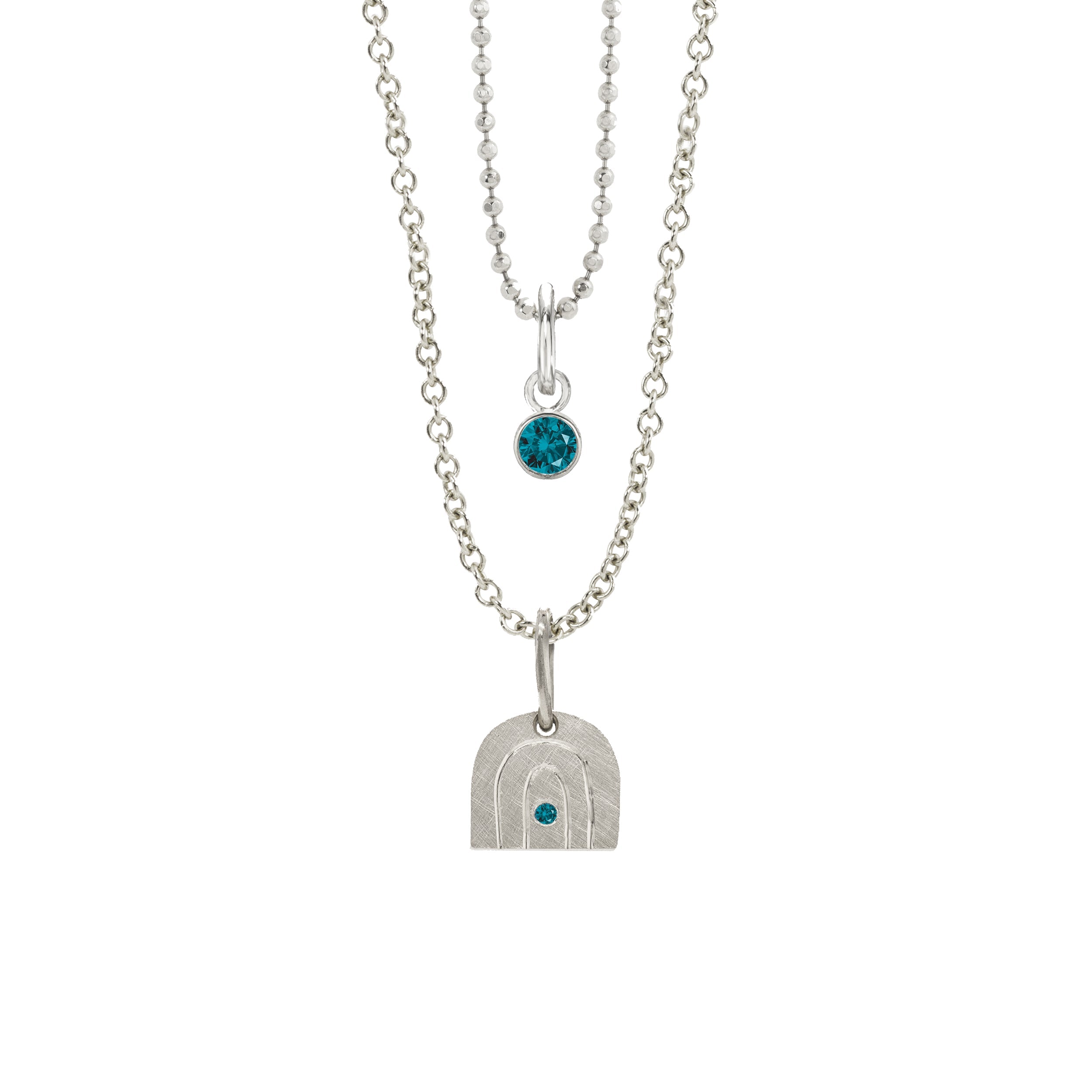 14k white gold rainbow pendant with a colored gemstone in the center on a rolo chain stacked with a bezel set colored gemstone on a diamond cut ball chain on a white background
