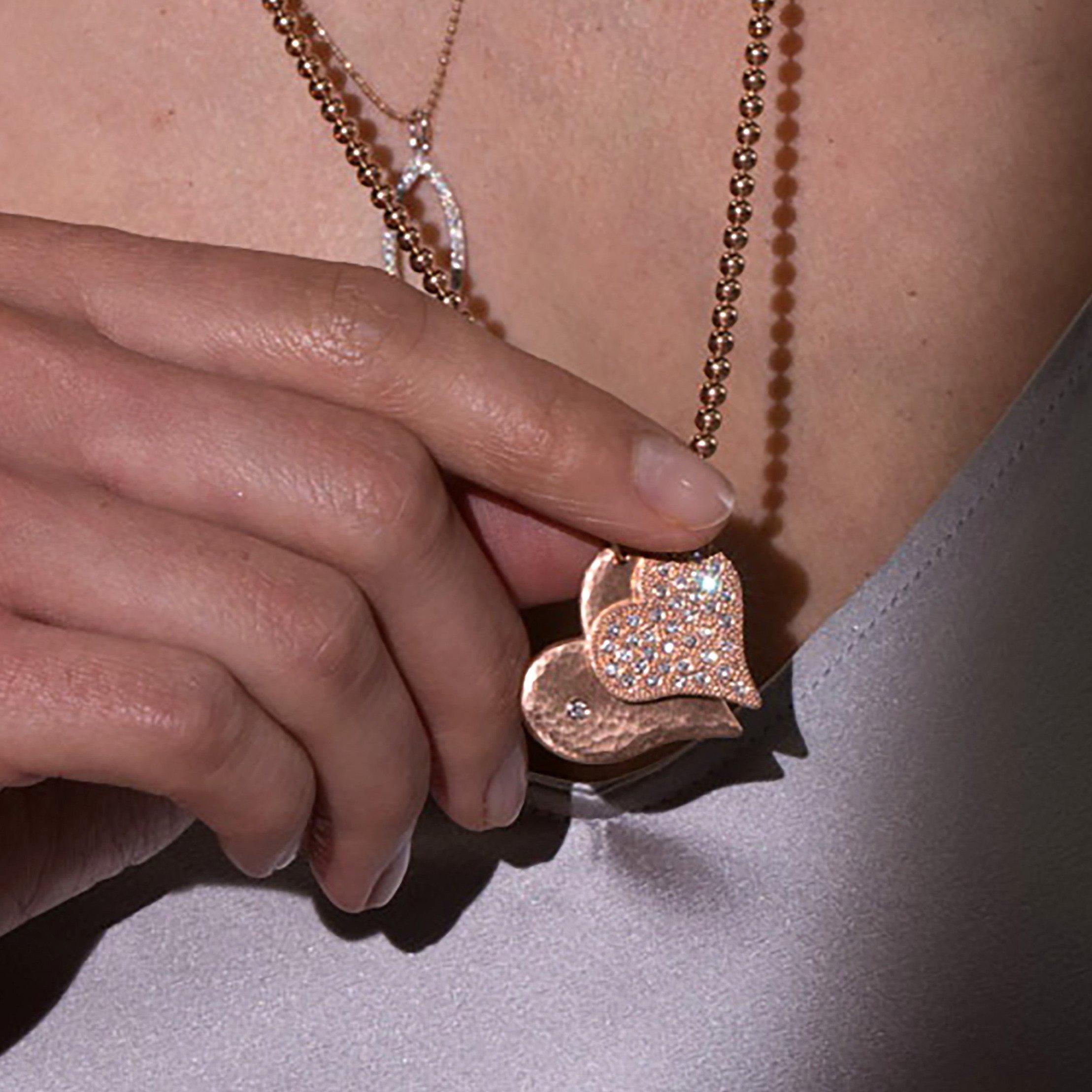 14k heart pendants featuring the lana in rose gold with a hammered finish and white diamond and the lava in rose gold with beaded textures and scattered white diamonds on a ball chain on model in lifestyle shot