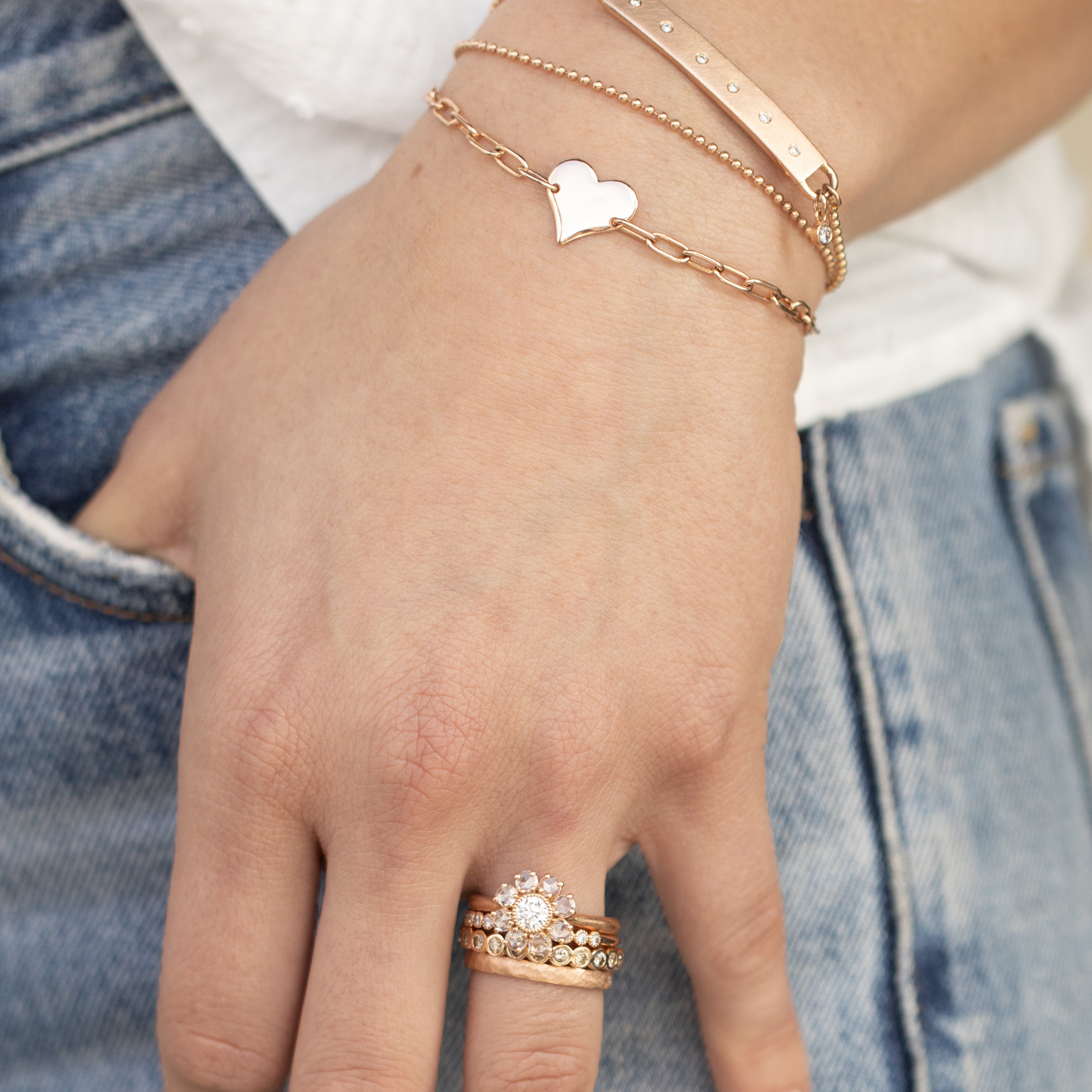 14k yellow gold heart bracelet with paperclip link chain stacked with wrap bracelet with white diamonds and bezi charm on ball chain on model in lifestyle shot