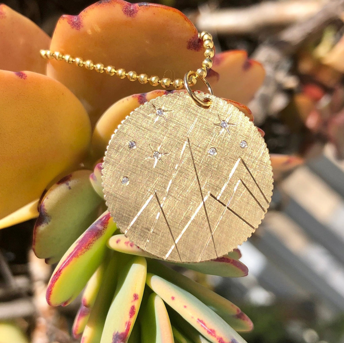 14k gold medallion pendant with etched mountains and white diamonds in lifestyle shot