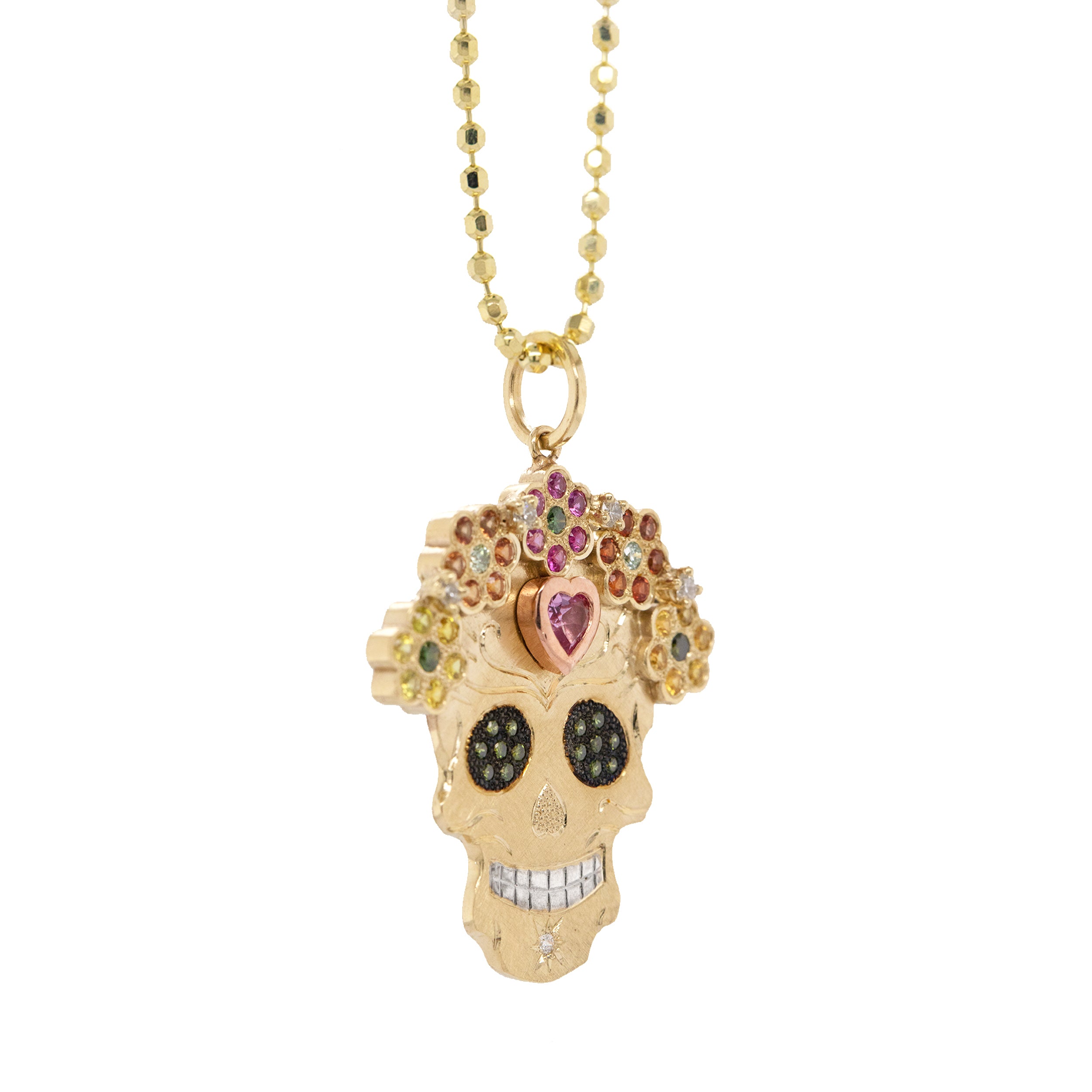 3/4 view of vibrant colorful Julez Bryant original Ghostrider Collection Mi Amore gemstone encrusted sugar skull extra large pendant. 14k solid yellow gold mixed diamond sapphires and Tzavorite. Fine detail engraving highlights features. Crown of flower clustered jewels in mixed colors. Rhodium blackened eyes with green Tzavorite pave set gemstone eyes. Large pink sapphire bezel set on forehead with rose gold border. Shown on 2.0mm ball chain.