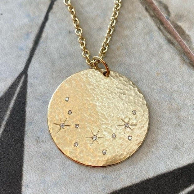 14k yellow gold round medallion with hammered finish and scattered white diamonds with hand etched starbursts on rolo chain on tile background