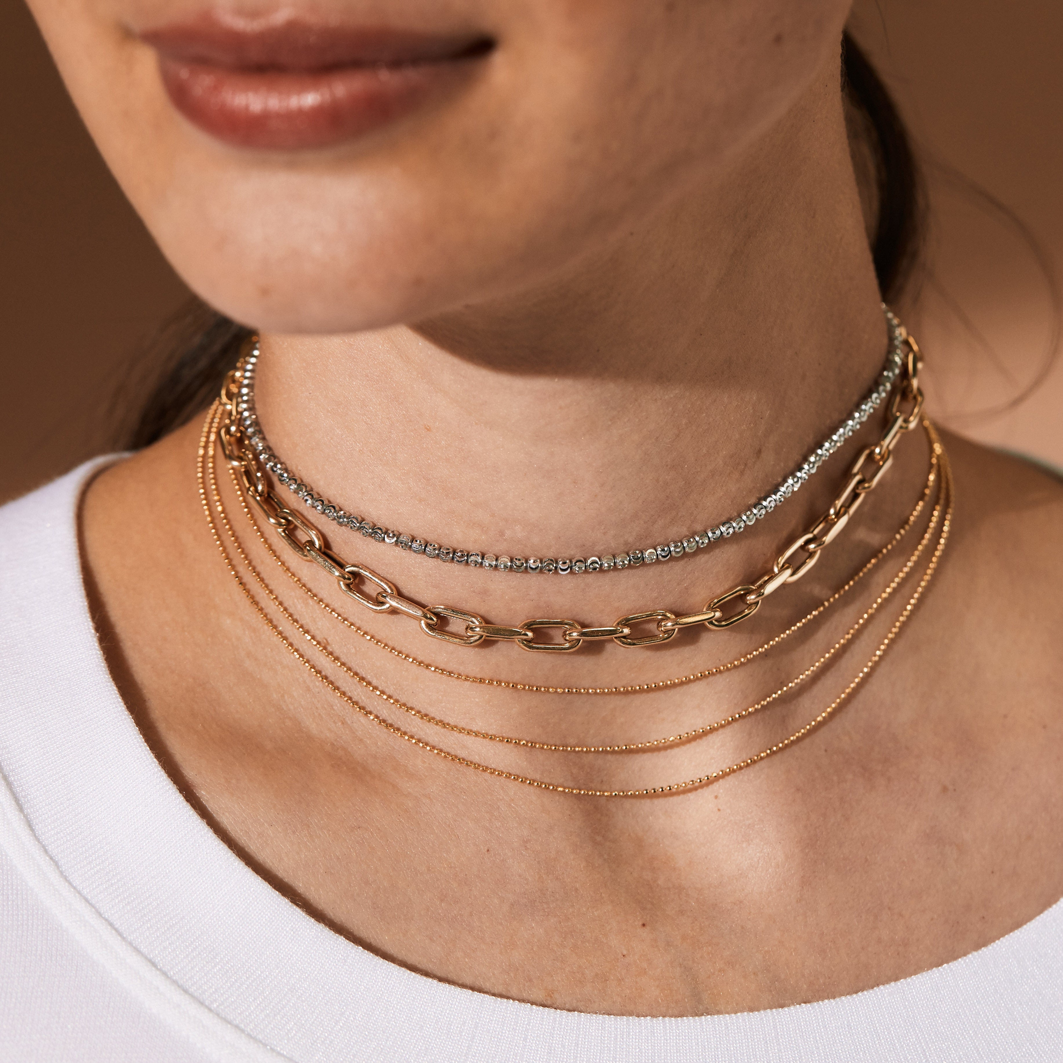 Close-up of a person wearing multiple choker length gold necklaces on a neutral background