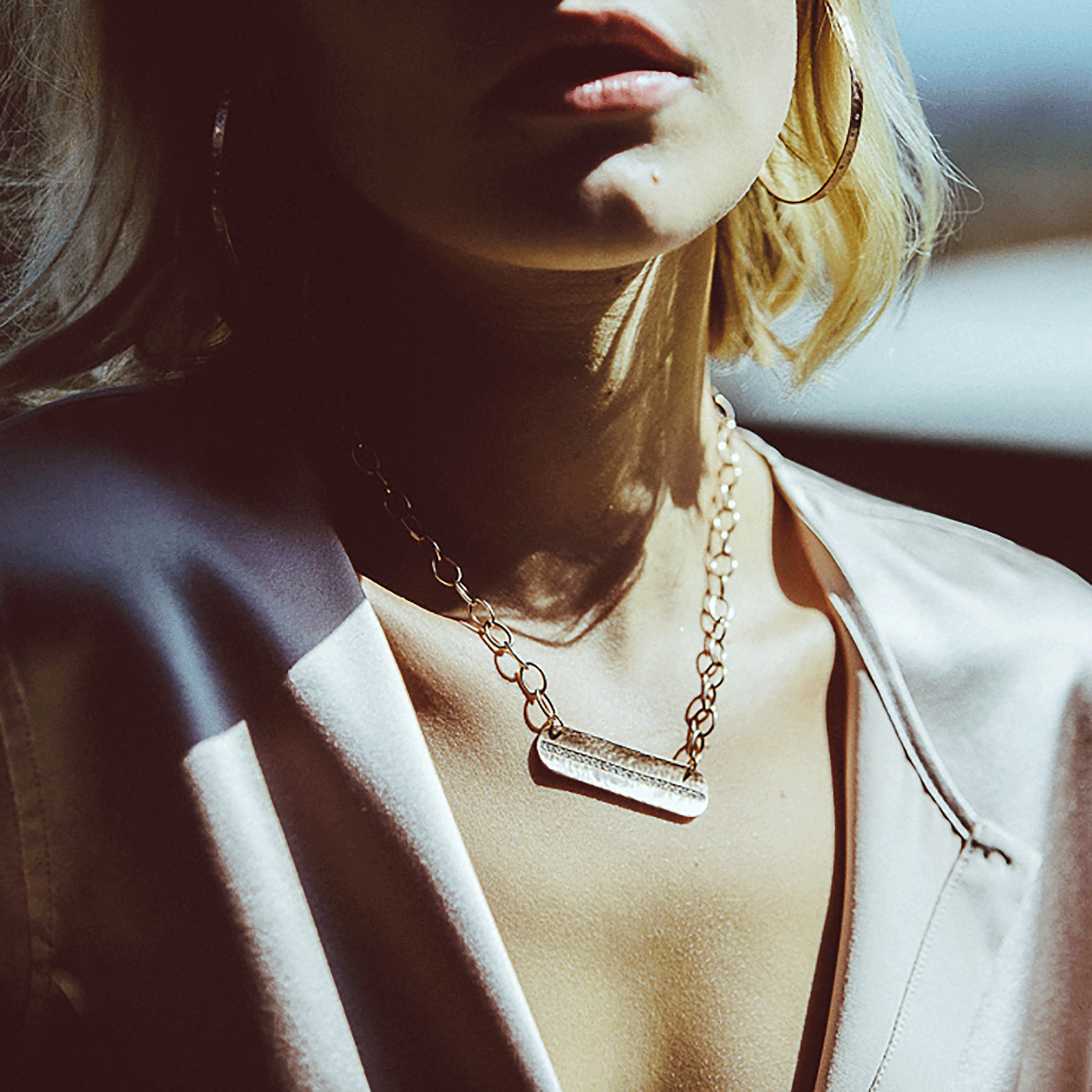 Close up of model wearing 14K yellow gold necklace with bar pendant with hammered texture featuring pave white diamonds hanging from large oval link chain on white background