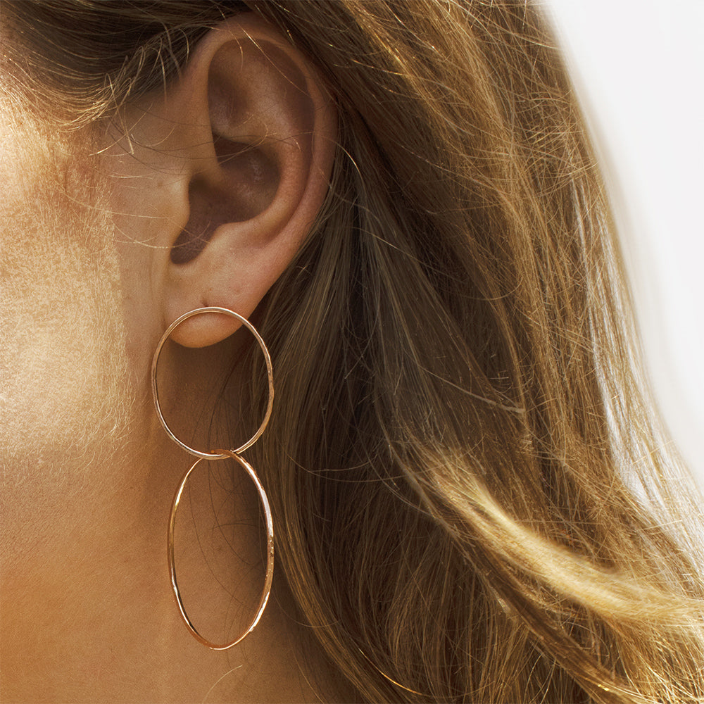 Close-up of an ear wearing a gold double hoop earring with blurred hair and background