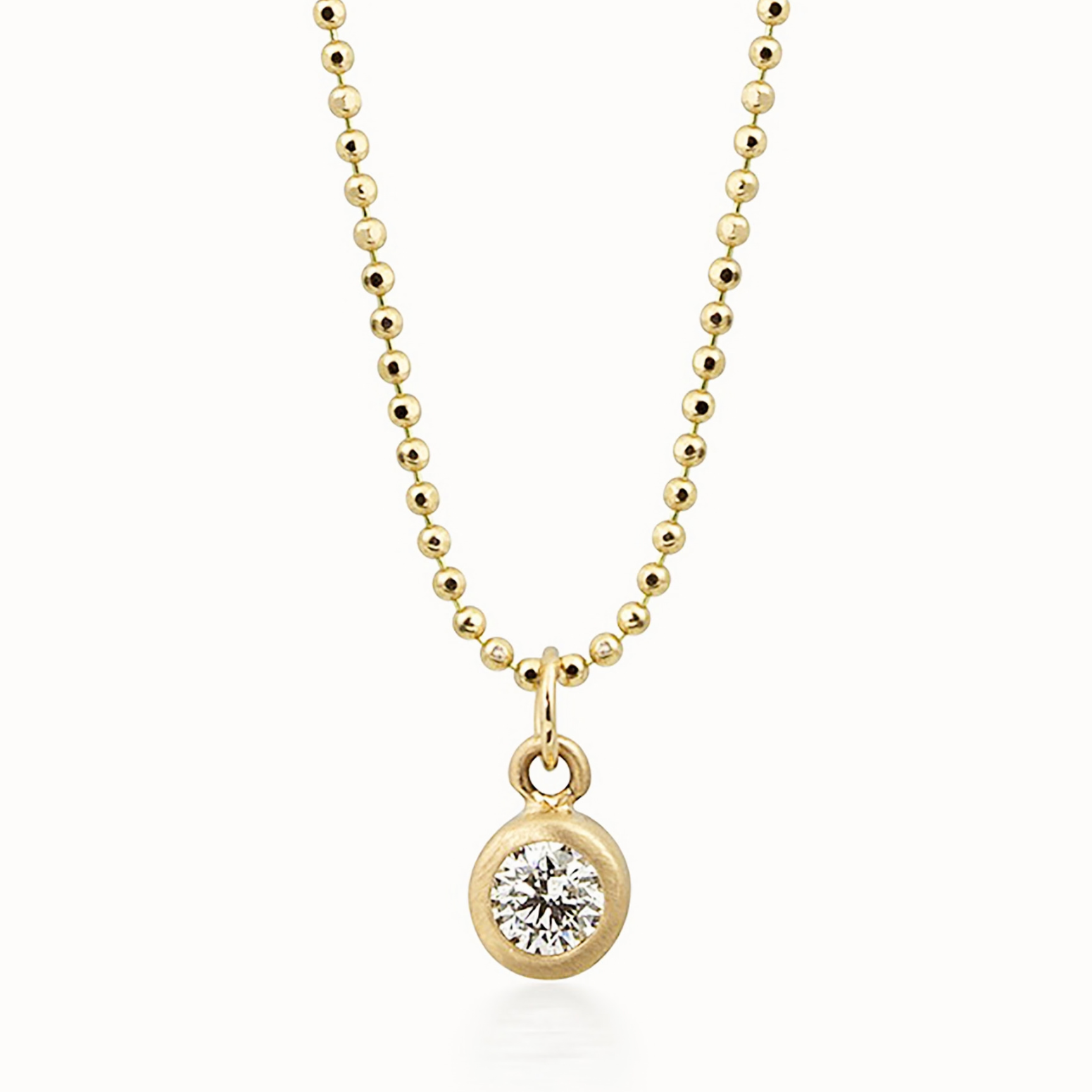 14k yellow gold bezel set diamond pendant on a diamond cut ball chain on a white background