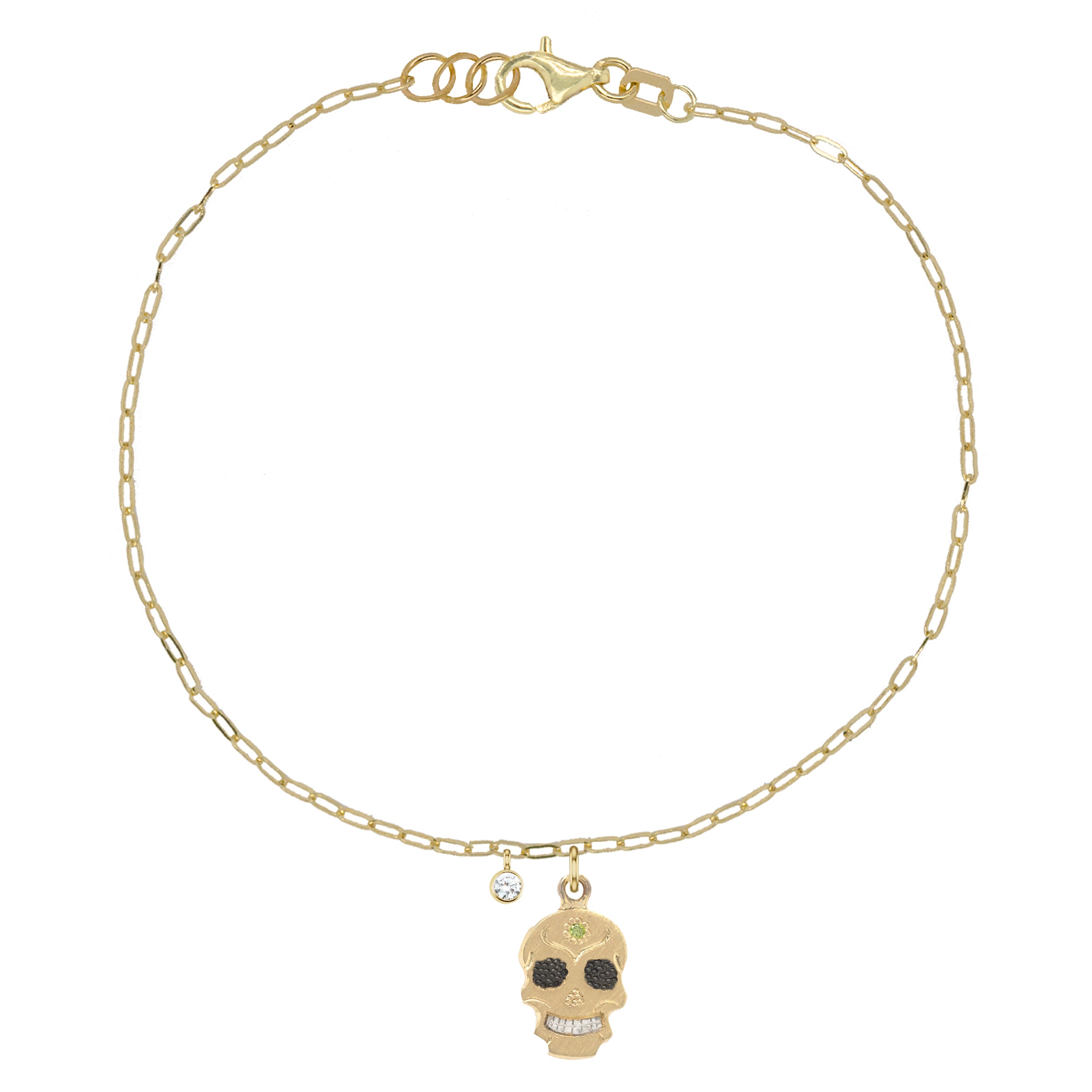 A gold bracelet featuring a tiny sugar skull charm and a sparkling gemstone dangle, on a thin link chain.
