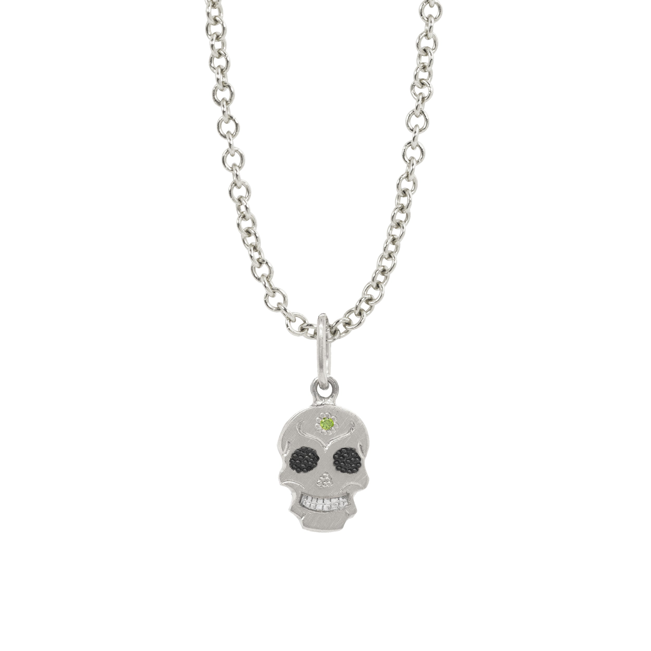 A Teeny Tiny Collection small 14k White gold candy skull charm on a round link rolo chain. Blackened rhodium eyes with black diamonds, floral detail on forehead with pave set green diamonds. Detailed engraved flourishes. Bright rhodium finish on teeth.