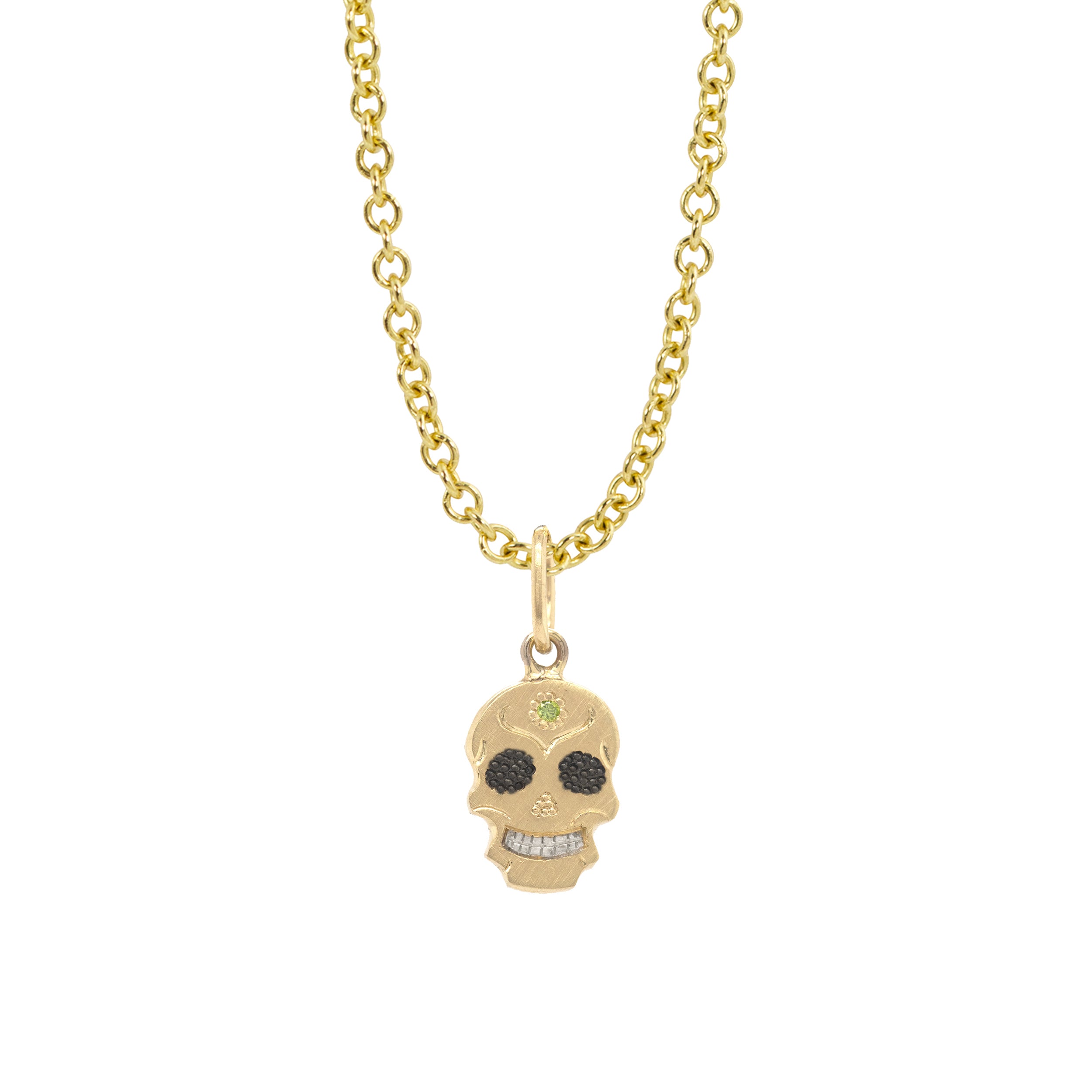 A Teeny Tiny collection gold charm in the shape of a sugar skull with a round apple green diamond in the center, displayed on a gold chain against a white background.