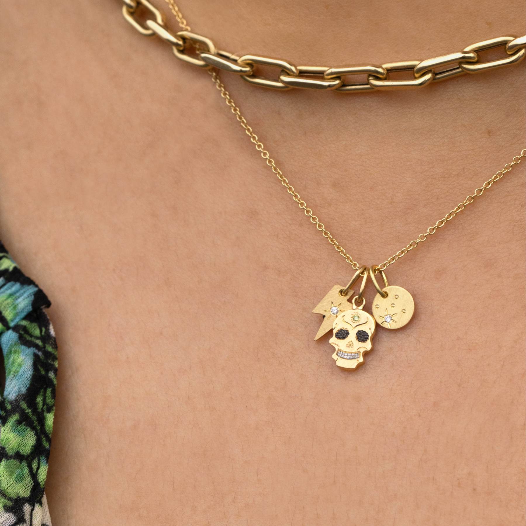 14k yellow gold skull pendant with blackened eyes and colored gemstones stacked with other teeny tiny charms on model in lifestyle shot