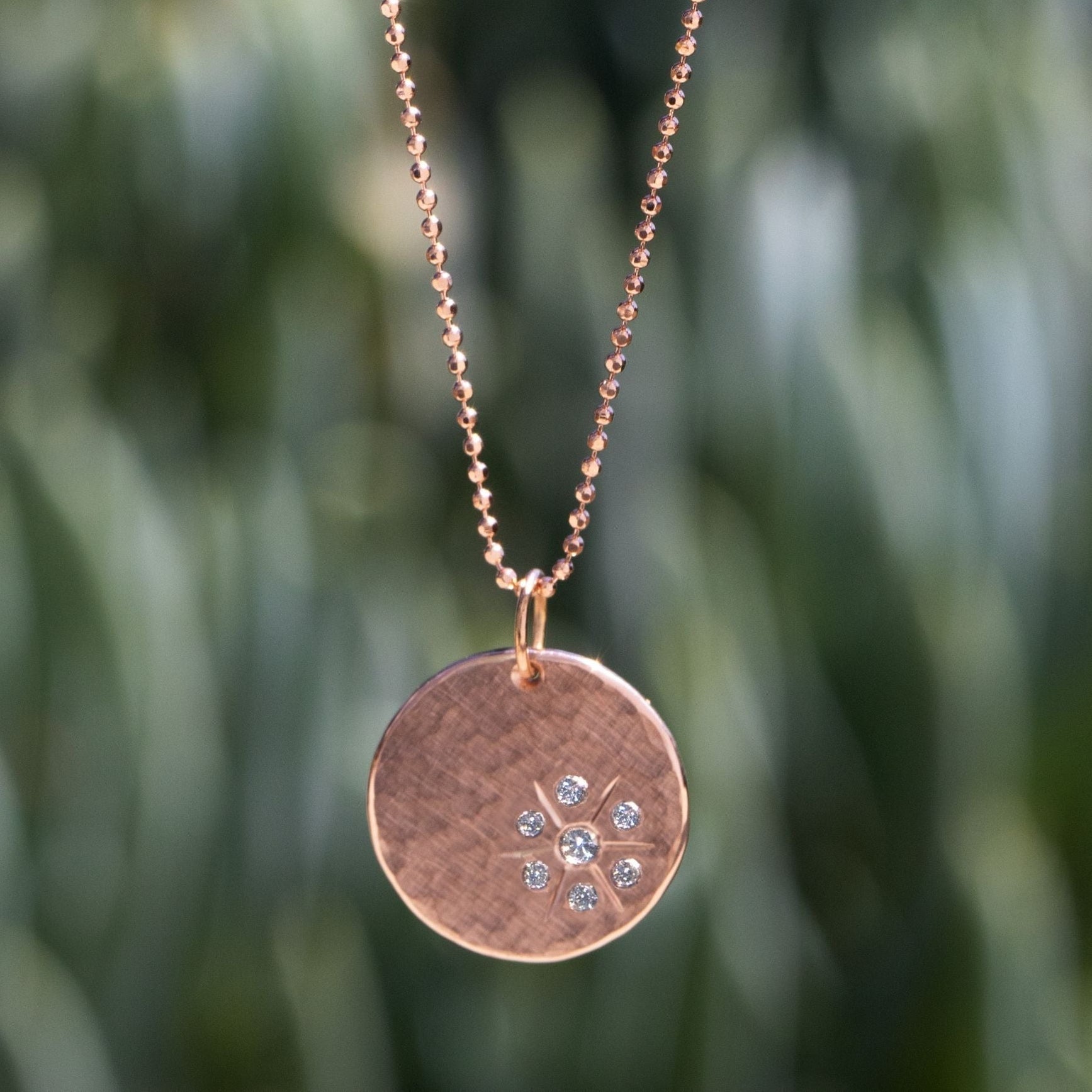 14k rose gold round hammered pendant with white diamond starburst on a natural background