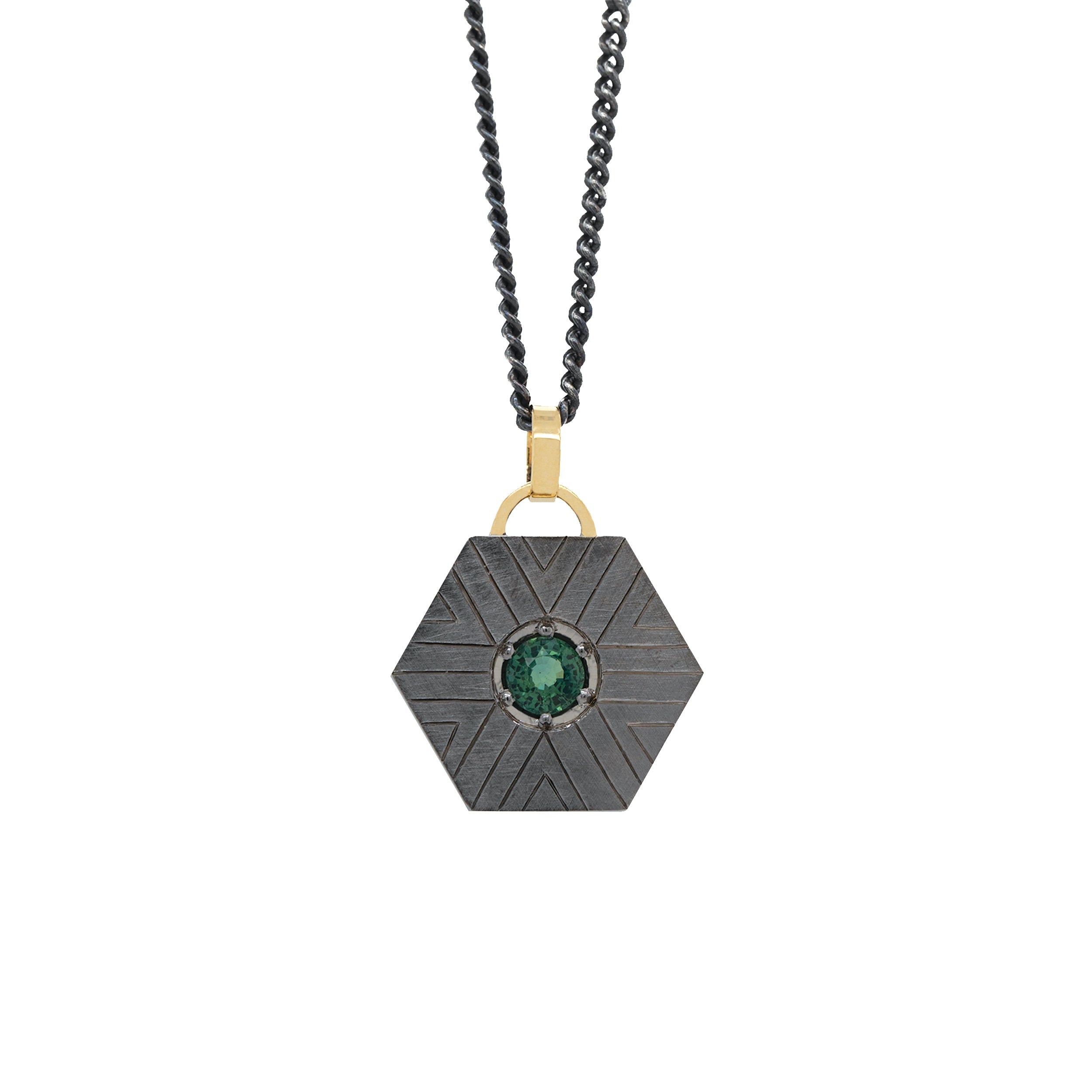 blackened sterling silver hexagonal pendant with geometric etching and a green sapphire with 14k yellow gold jump ring on white background