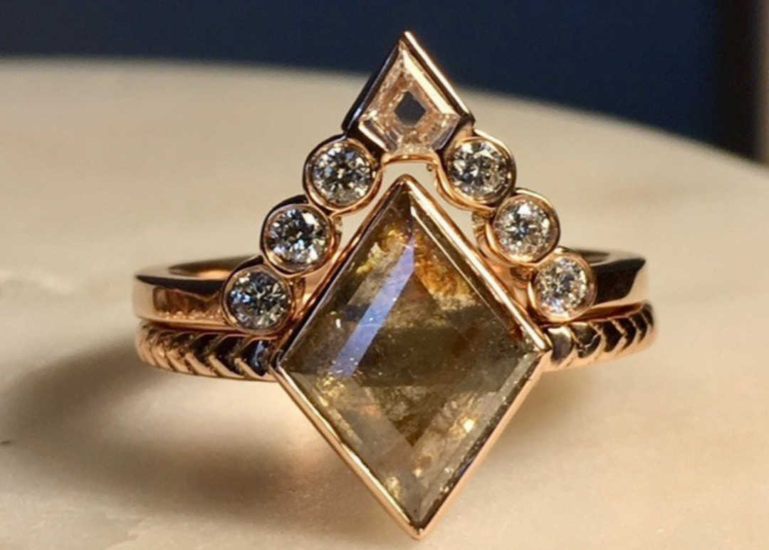 Rose gold ring with a large rectangular stone and smaller stones on a beige surface