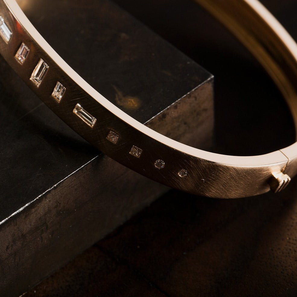 18k yellow gold hinged bangle bracelet with baguette and round white diamonds on dark background