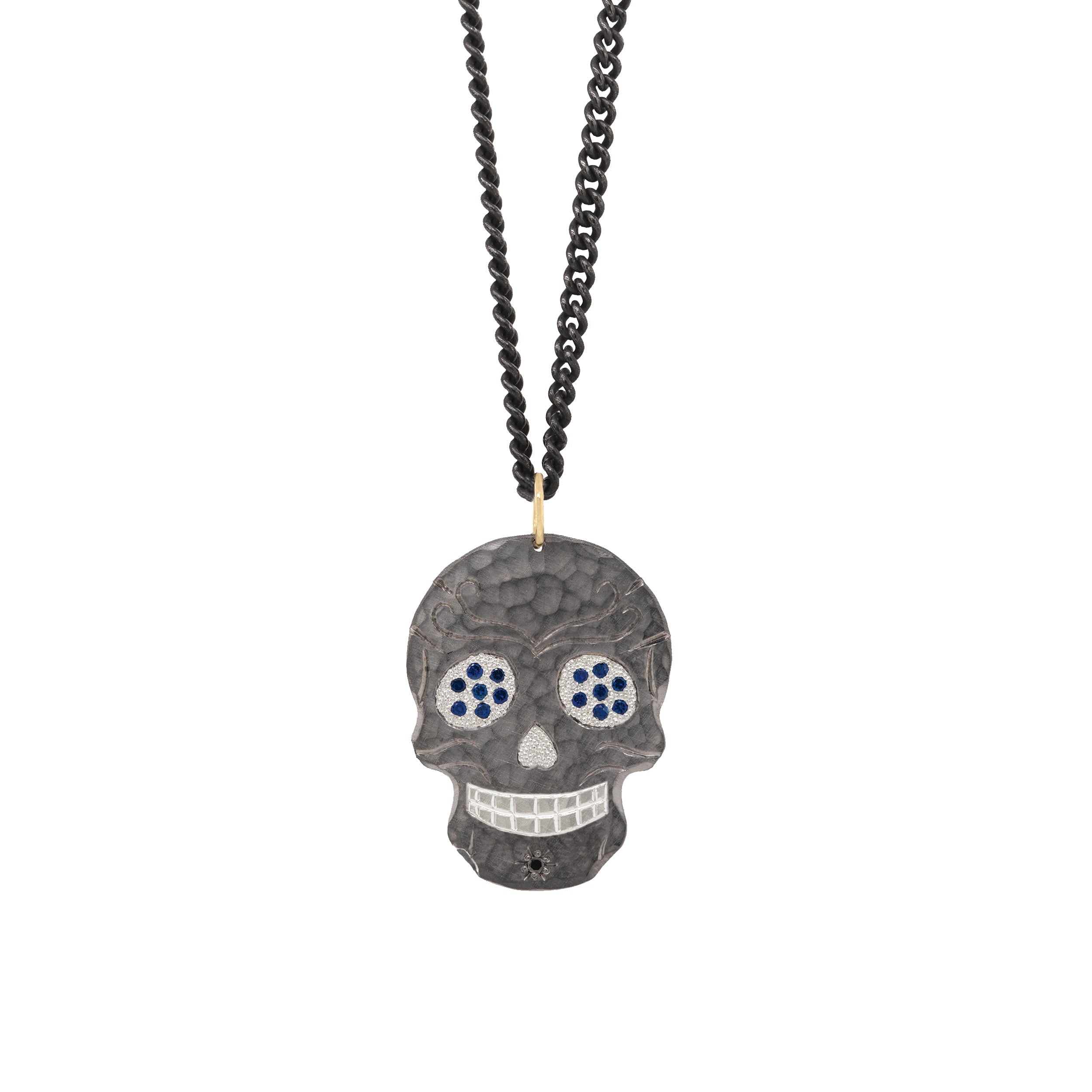 blackened sterling silver ghostrider pendant with hammered finish and beaded texture eyes with blue sapphires and hand etched details on white background