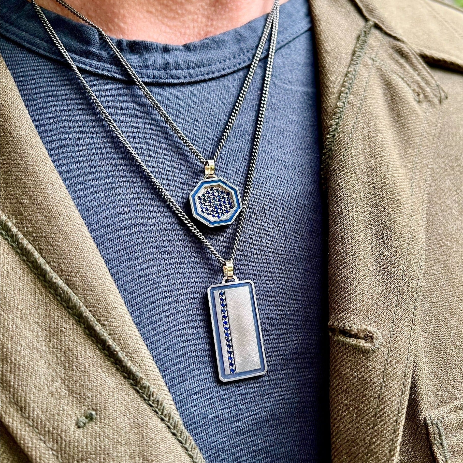 blackened sterling silver rectangular pendant with colored enamel and colored gemstone line with 14k yellow gold jump ring stacked with blackened sterling silver octagon pendant with colored enamel border and colored gemstones with 14k yellow gold jump ring on model in lifestyle shot