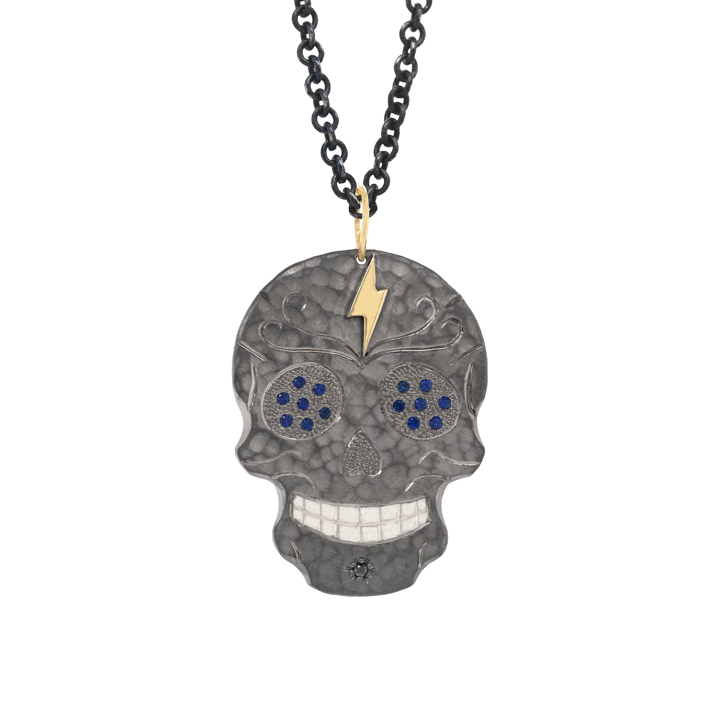 blackened sterling silver ghostrider pendant with hammered finish and hand etched details with beaded texture and blue sapphire eyes and 14k yellow gold accents on white background