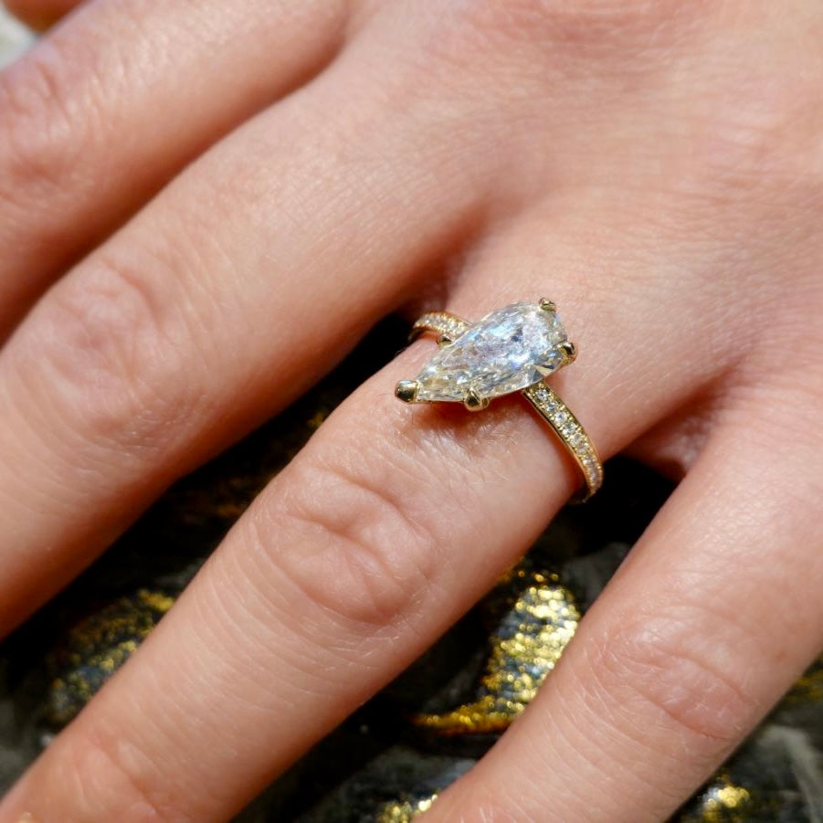 14k yellow gold ring with a large teardrop shaped diamond set tilted with milgrain  ernity band shown on a models hand