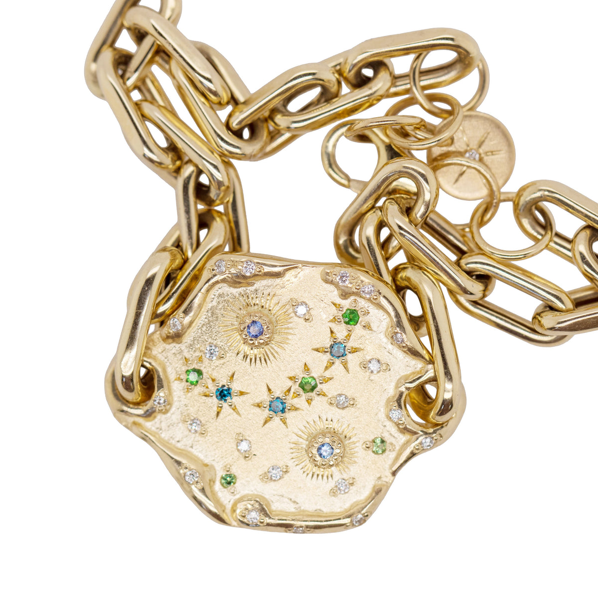 Close-up of the Bleu small 14k yellow gold charm chain bracelet, showing the starburst medallion charm set with blue sapphires, green tsavorites, and diamonds, alongside two engraved star disc charms.