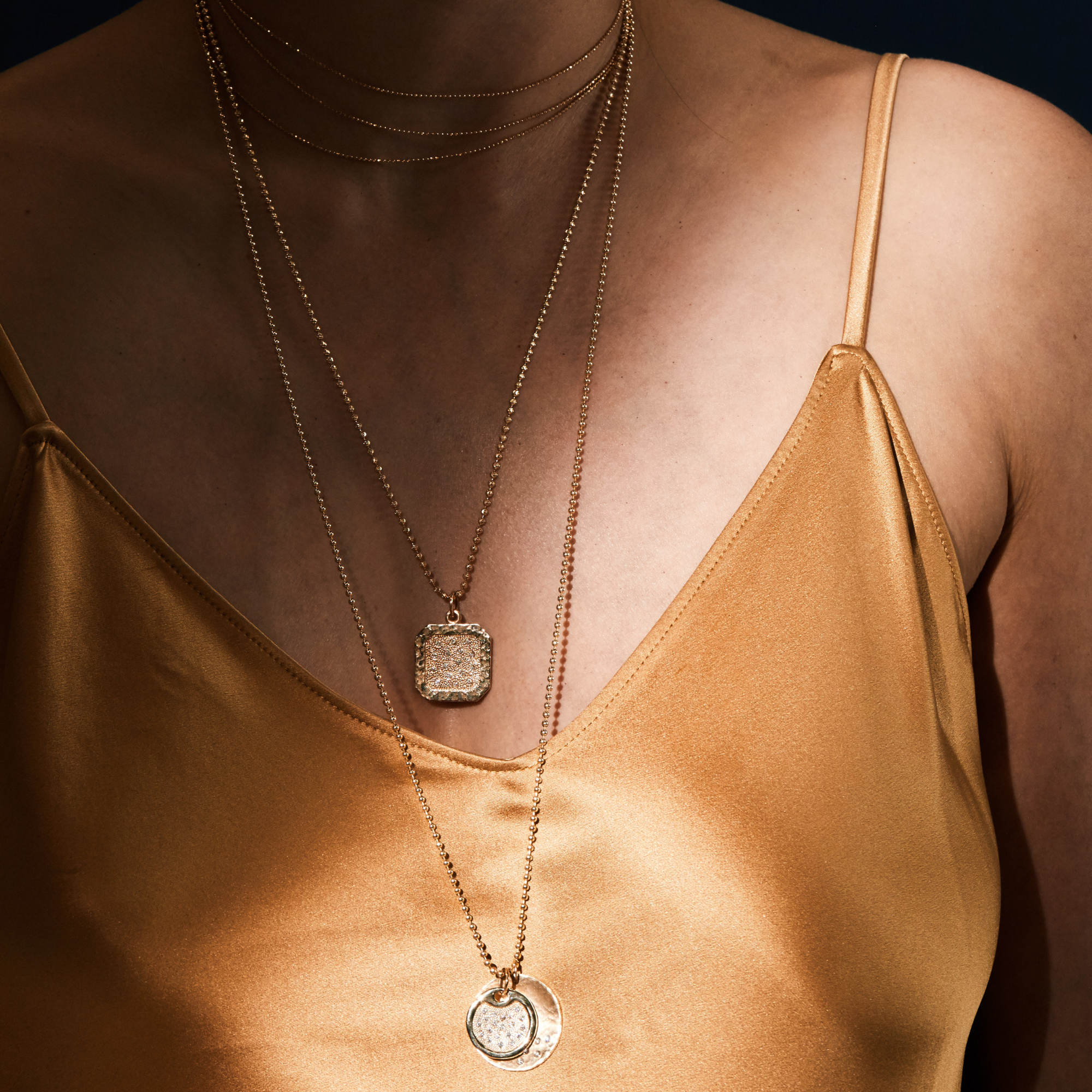 14k gold necklace stack including chai necklace with square beaded dogtag pendant with white diamonds on a diamond cut ball chain and the dena and megg pendants on a diamond cut ball chain on model in lifestyle shot