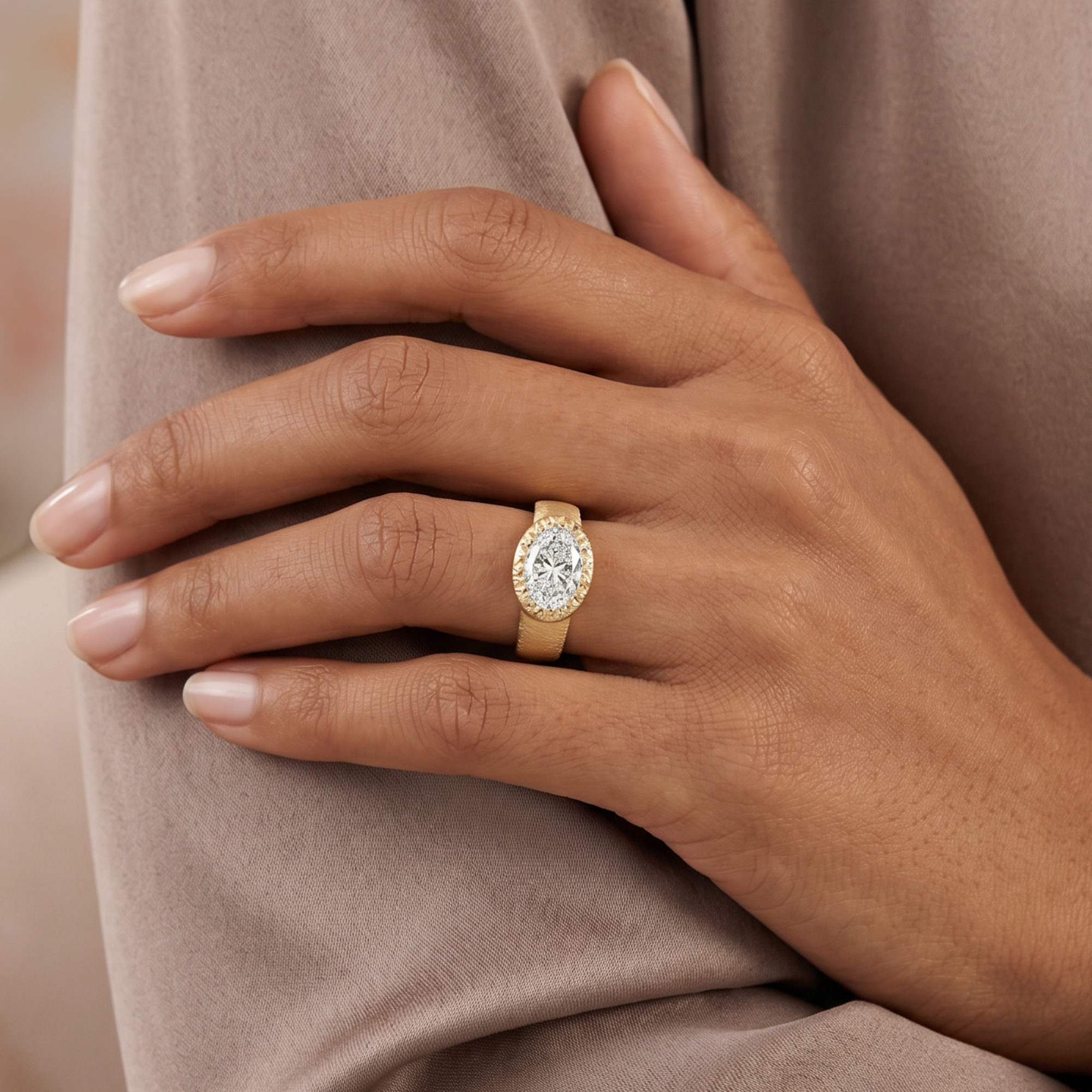 Chunky wide band east-west oval bezel solitaire diamond engagement ring with textured finish in 14k yellow gold, worn on a model's hand
