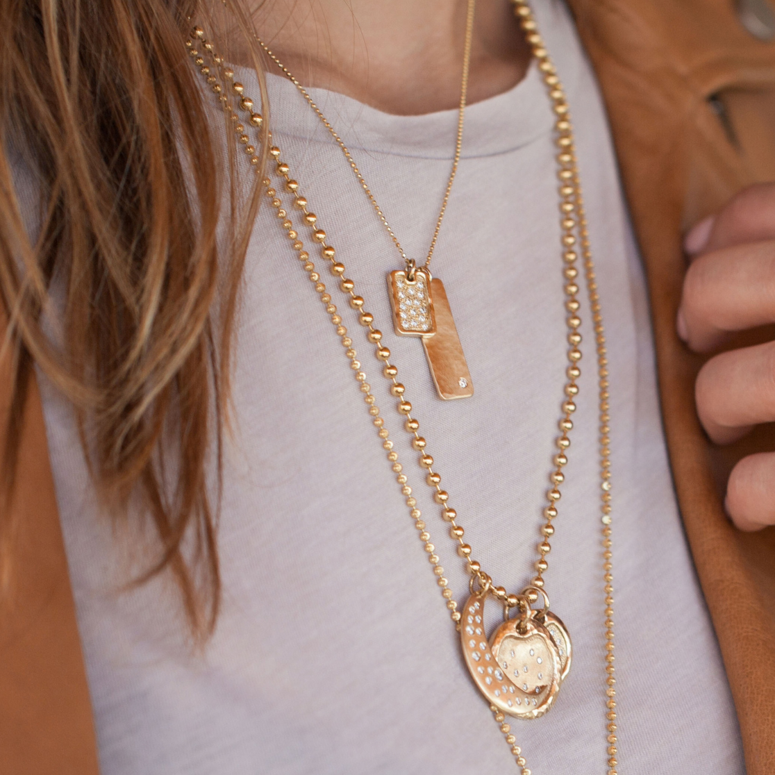 Layered 14k yellow gold white diamond  necklaces featuring dog tag and moon design pendants, jewelry by Julez Bryant close up on model lifestyle shot